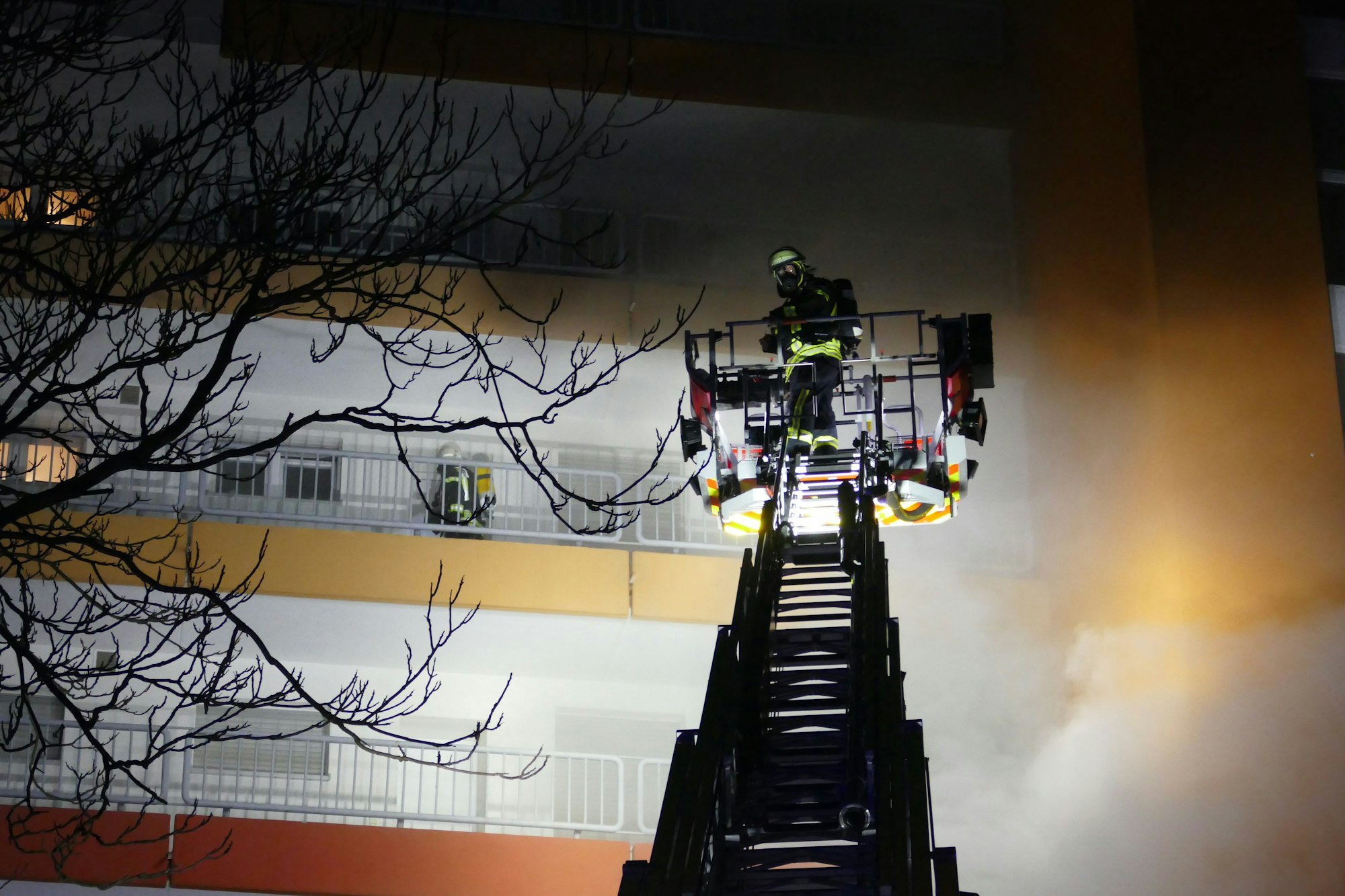 Ein Feuerwehrmann im Einsatz auf einem Kran bei einem Hochhaus mit dichter Rauchentwicklung