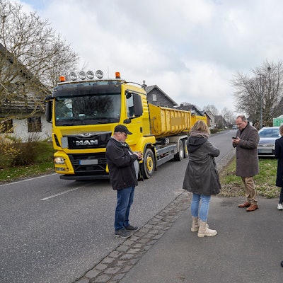 Während die Besucher am Straßenrand stehen, rollt ein Lastwagen mit Anhänger auf dem Mittelstreifen durch den Ort
