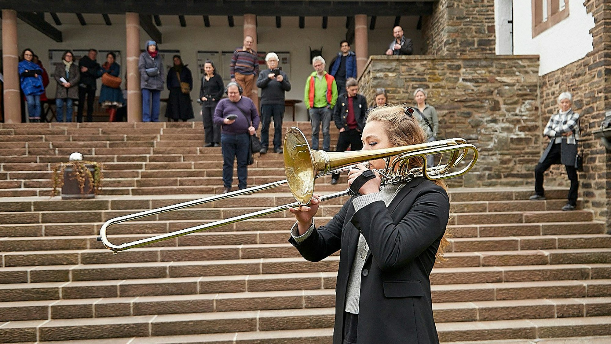 Im Vordergrund ist die Musikerin mit ihrer Bassposaune zu sehen, auf den Stufen dahinter lauschen die Besucher.