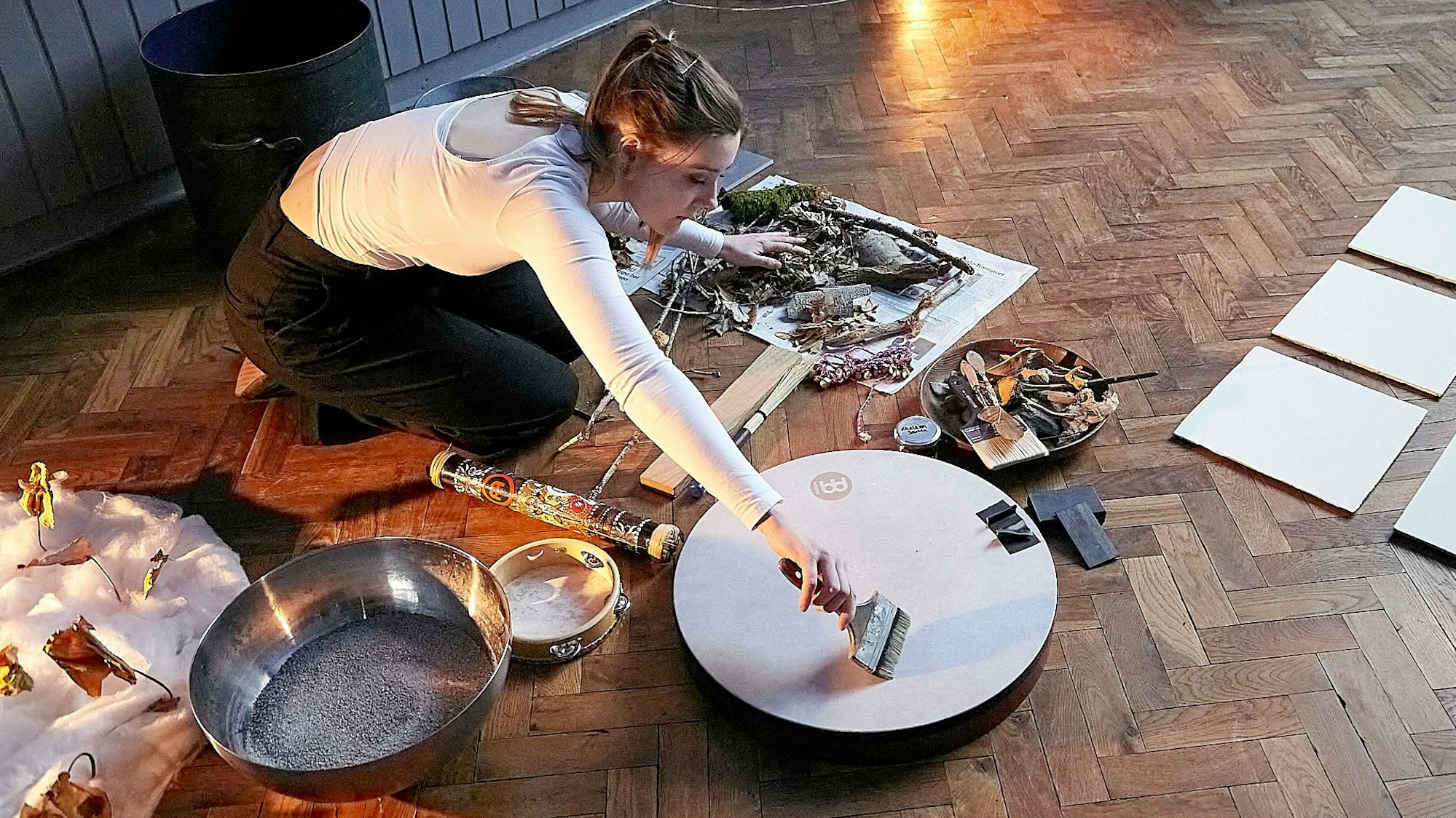 Die Musikerin streicht mit einem Pinsel über eine flache Rahmentrommel, während sie mit der anderen Hand in Zweigen und Blättern raschelt.