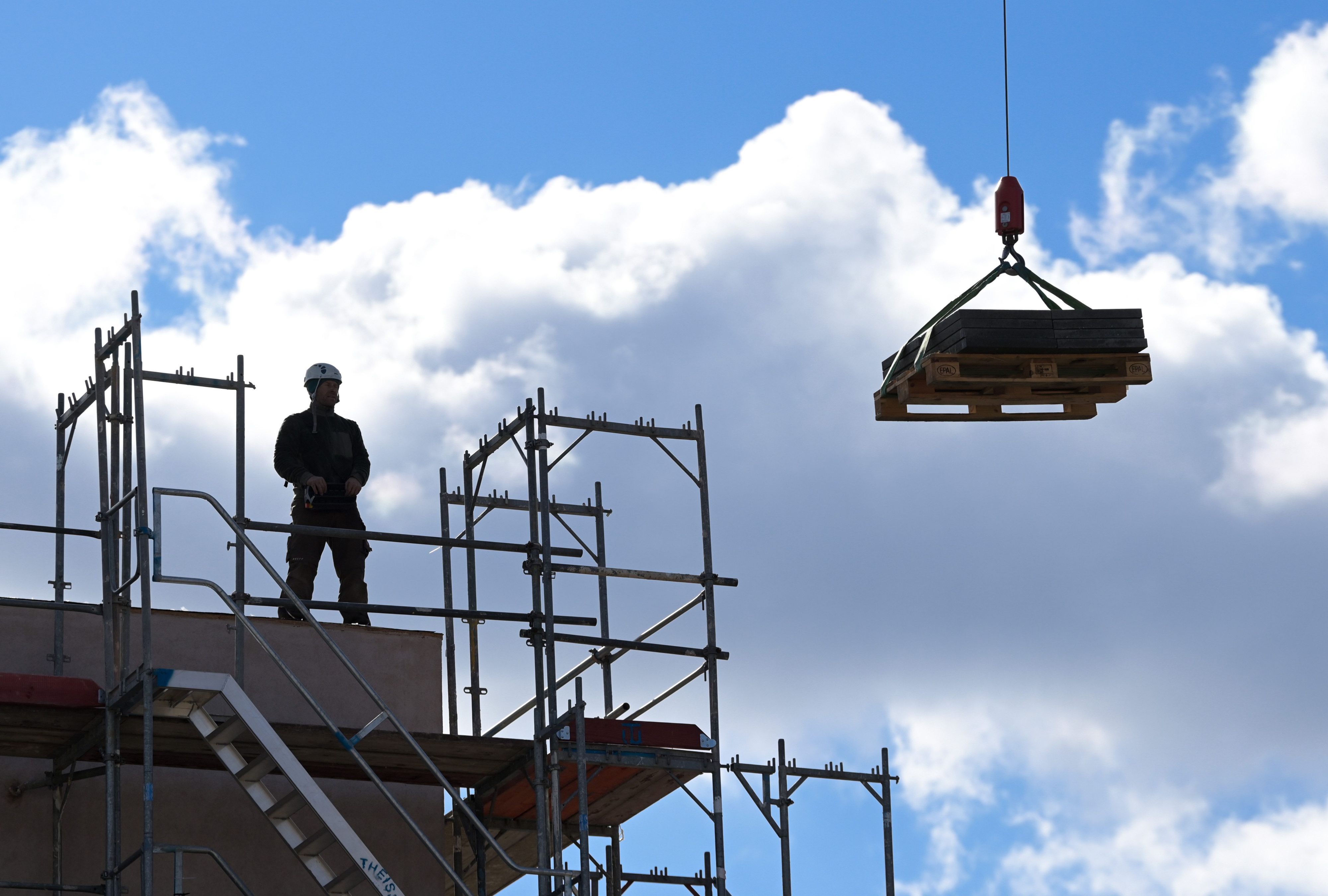 Ein Arbeiter dirigiert auf einer Baustelle einen Kran.
