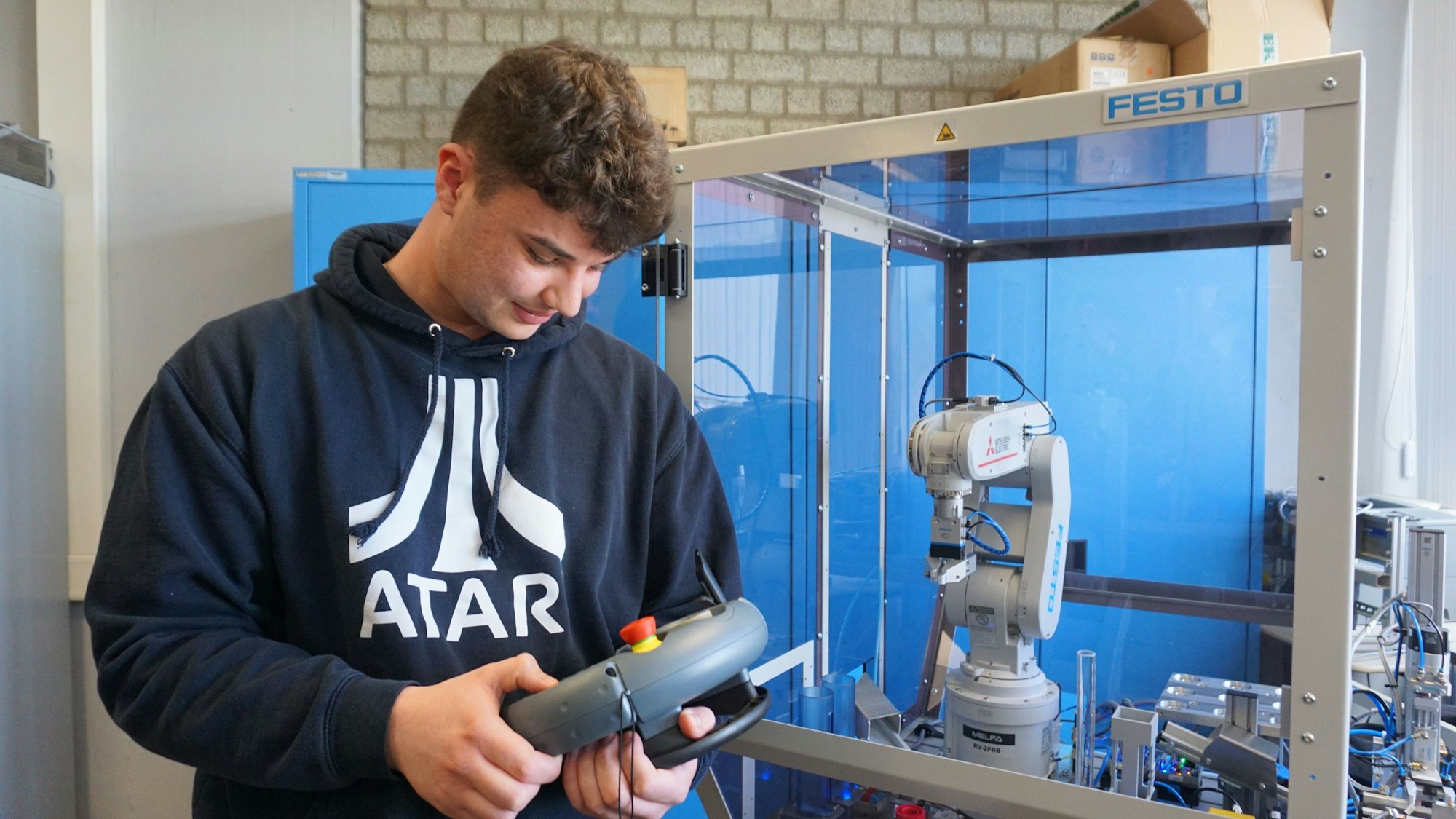 Berufsschüler Liam Allen führt die neue Robotik-Anlage am Thomas Esser Berufskolleg vor.