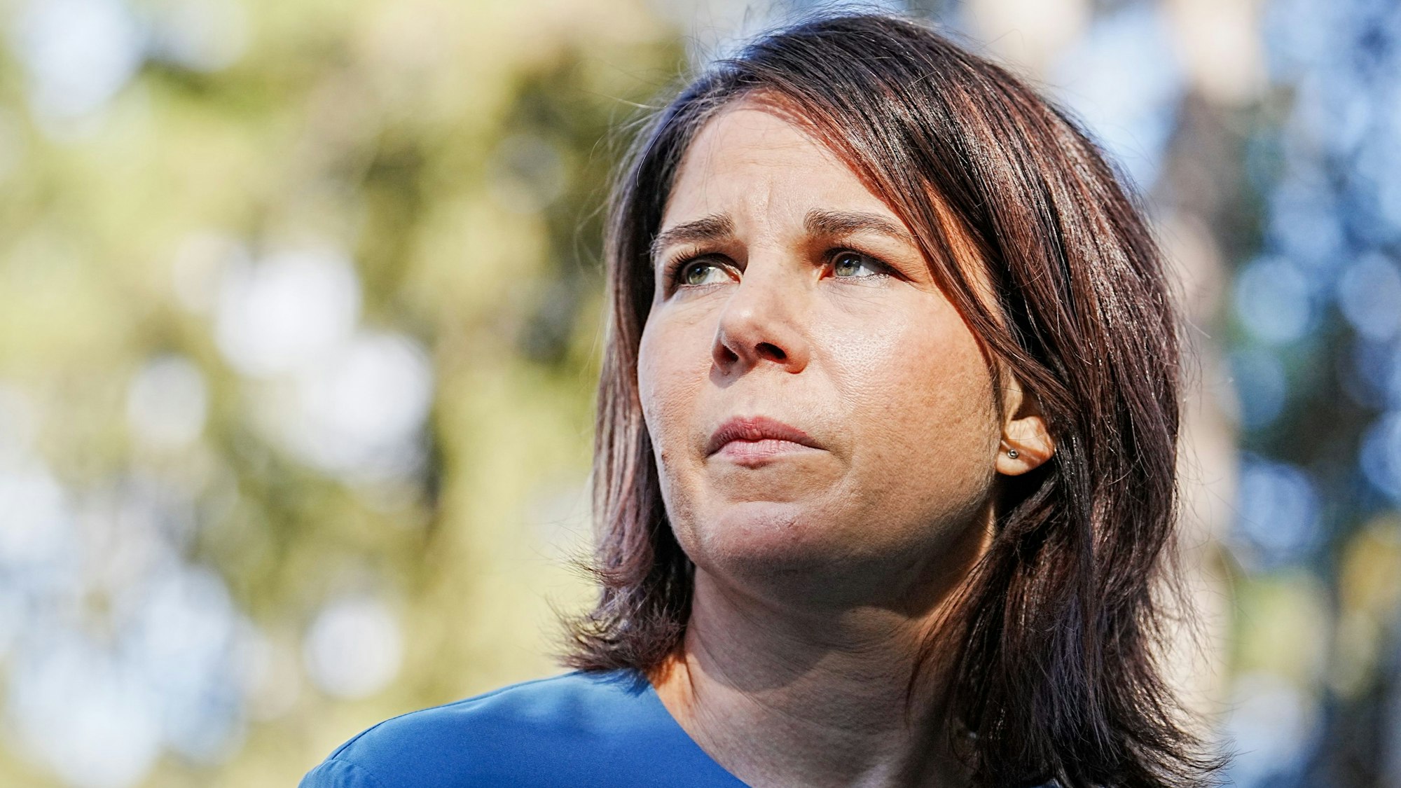 Bundesaußenministerin Annalena Baerbock (Grüne) blickt links neben die Kamera. Hinter der Politikerin ist unscharf ein Baum zu erkennen.