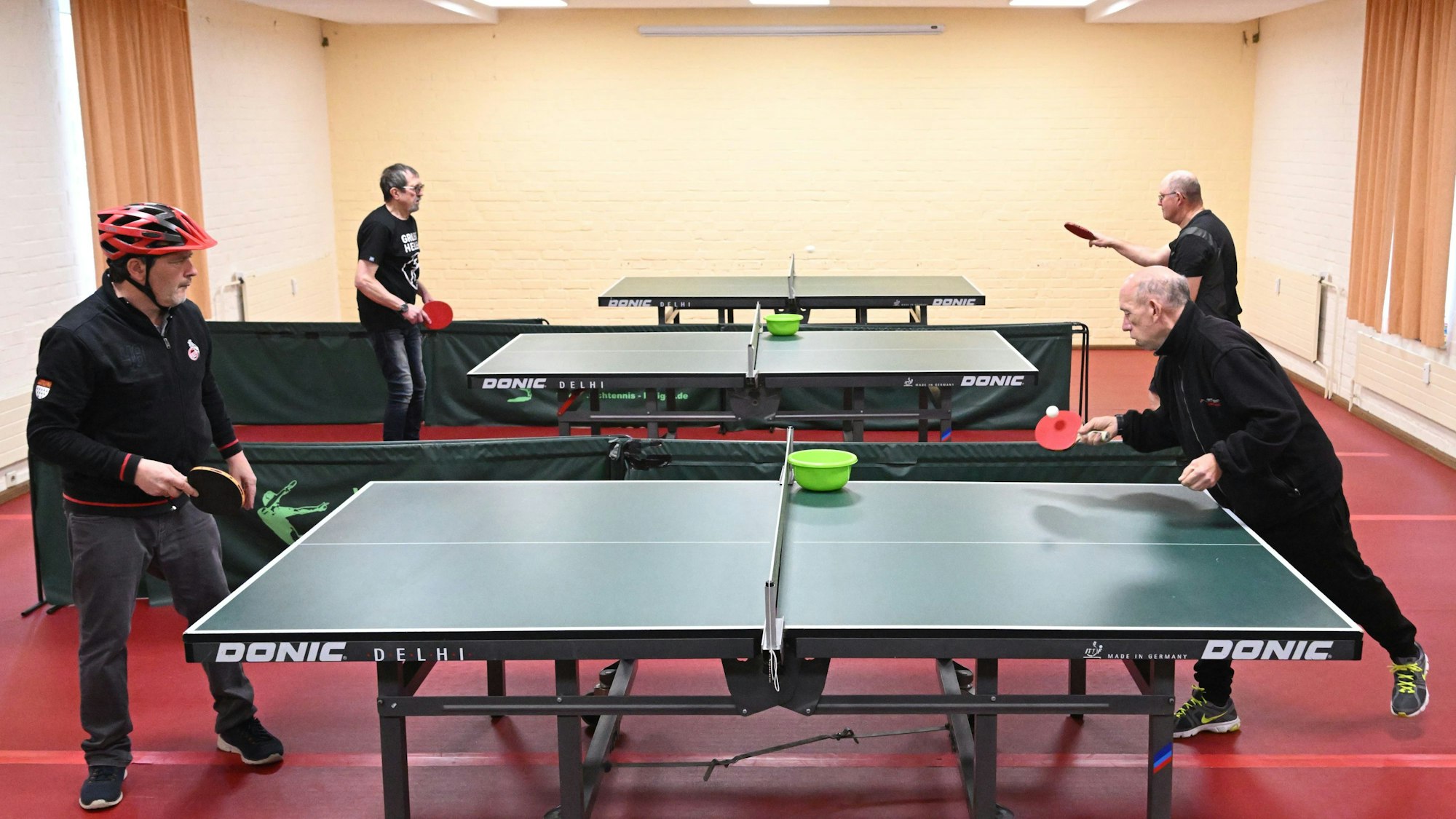 Vier Menschen spielen an zwei Tischtennisplatten Tischtennis.