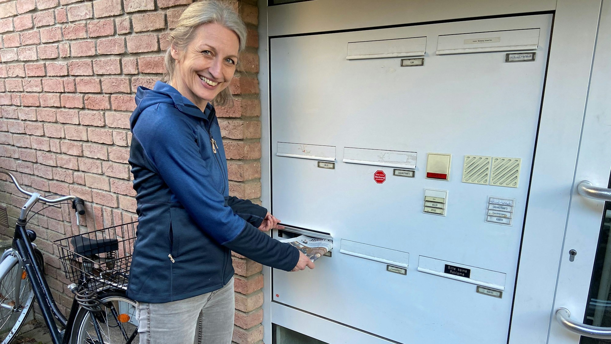 Die Zustellerin steckt eine Zeitung in den Briefkasten.