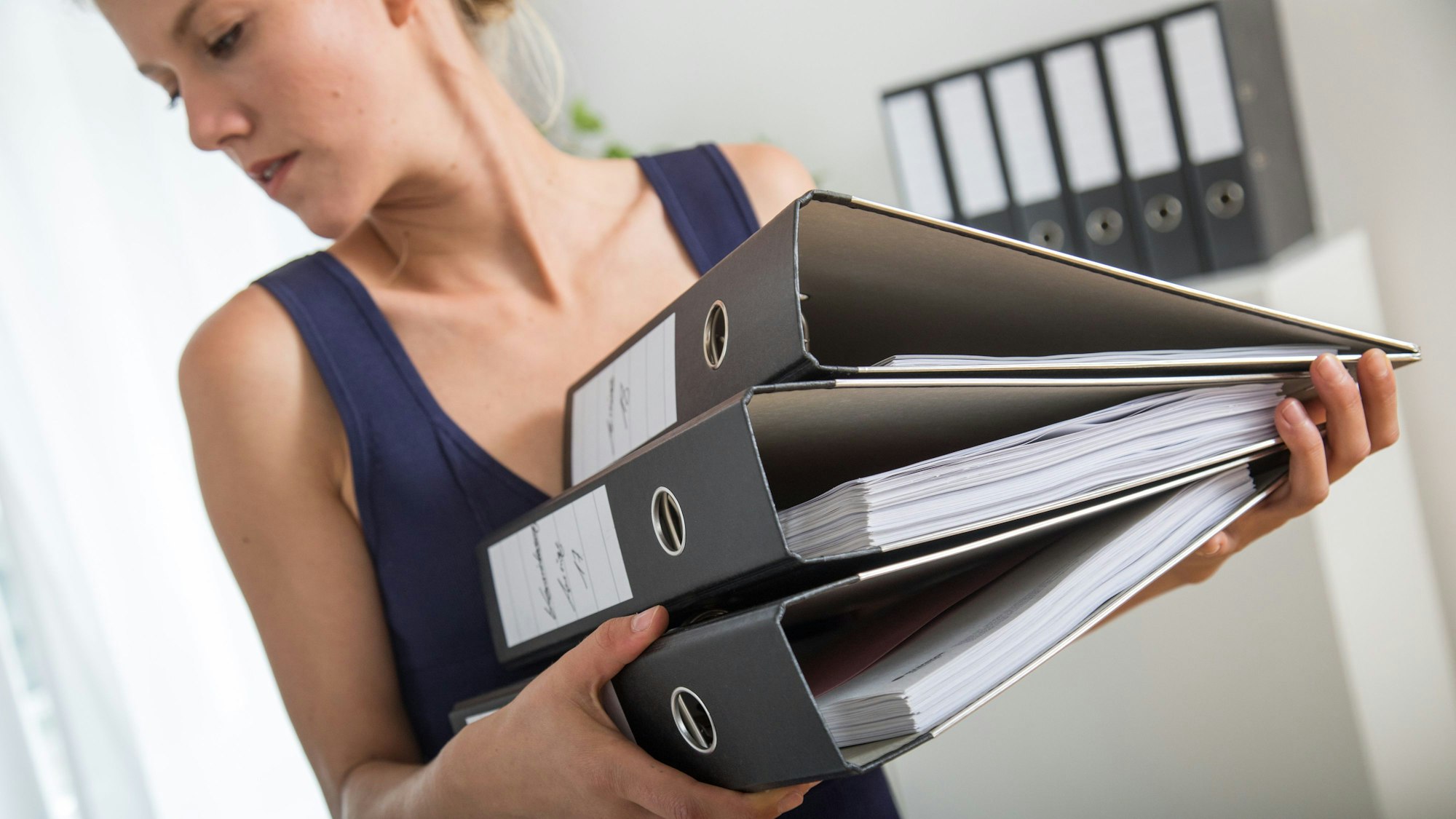 Eine Frau hält drei Aktenordner in den Armen