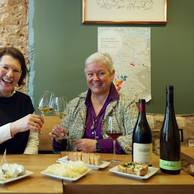 Zwei Frauen sitzen an einem gedeckten Tisch und prosten sich mit Weißwein zu