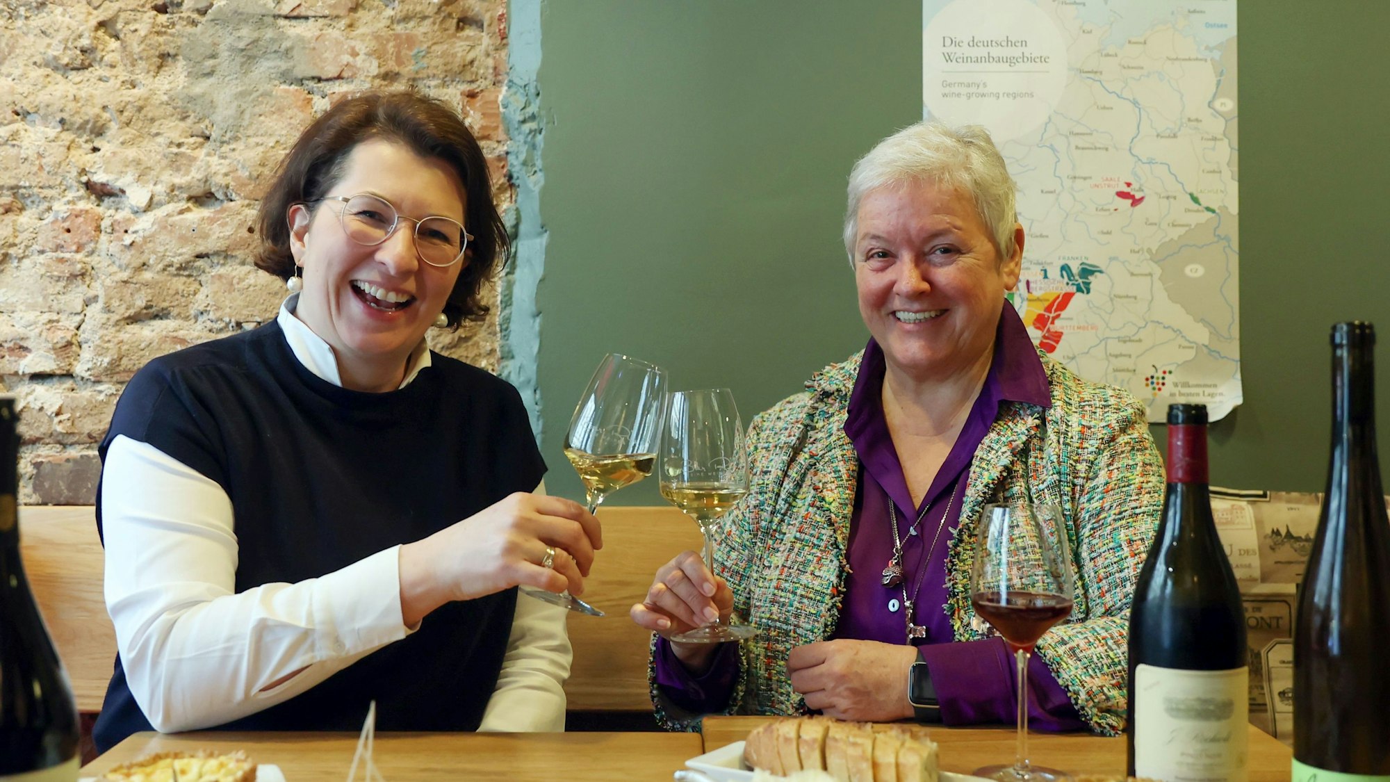 Zwei Frauen sitzen an einem gedeckten Tisch und prosten sich mit Weißwein zu