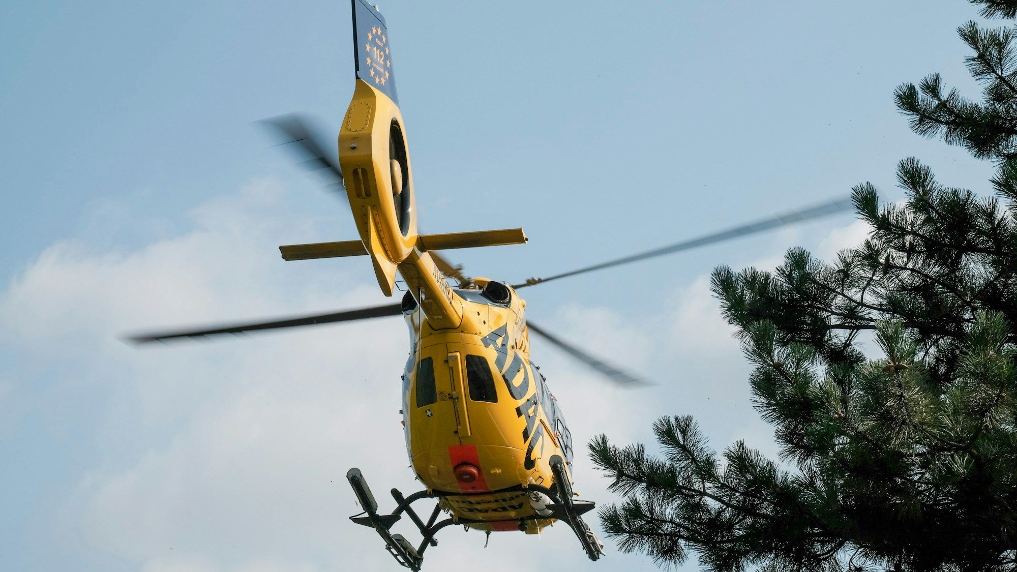 Ein gelber Rettungshubschrauber des ADAC von unten fotografiert.