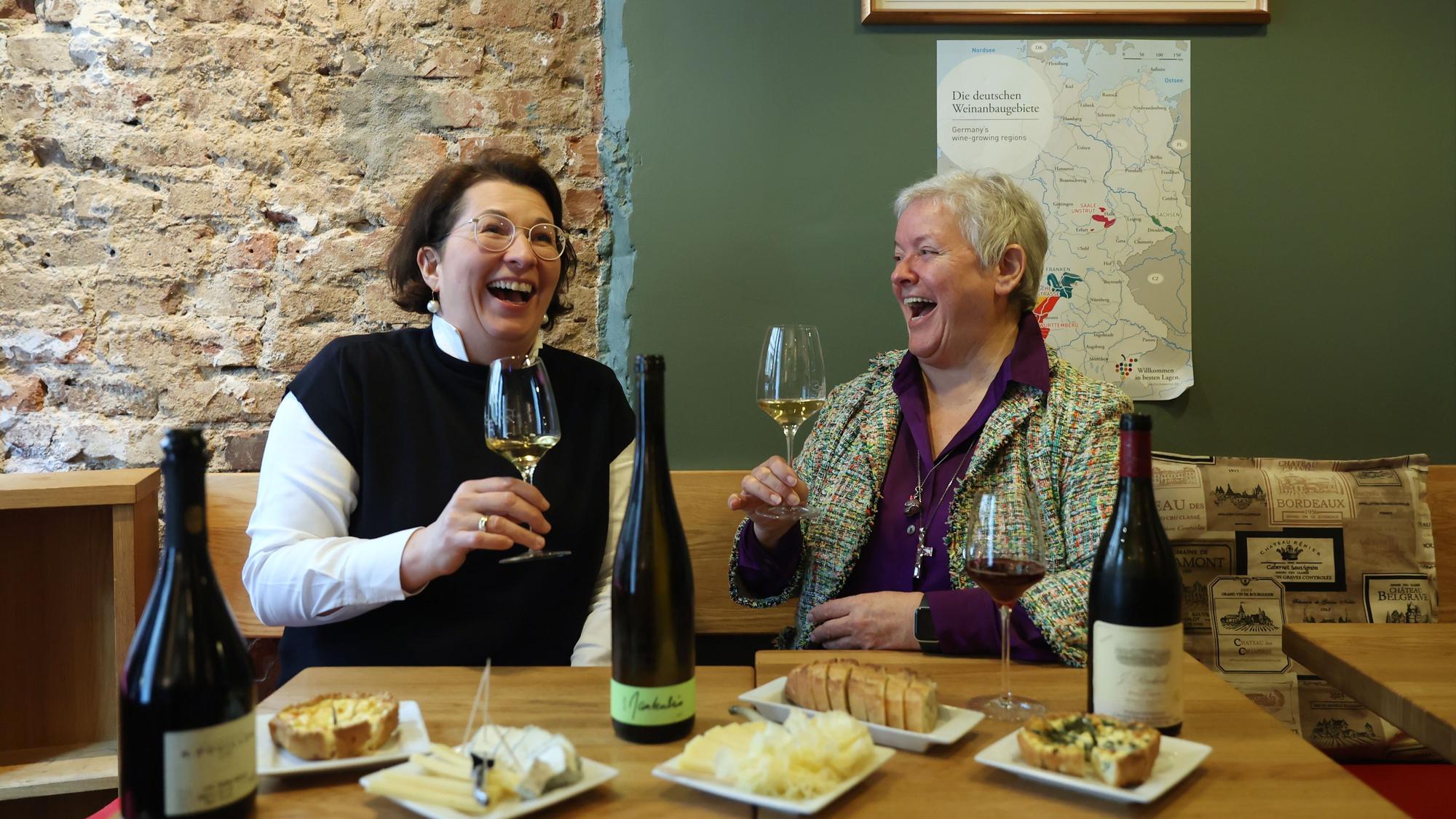 zwei Frauen sitzen mit einem Glas Wein an einem Tisch und lachen
