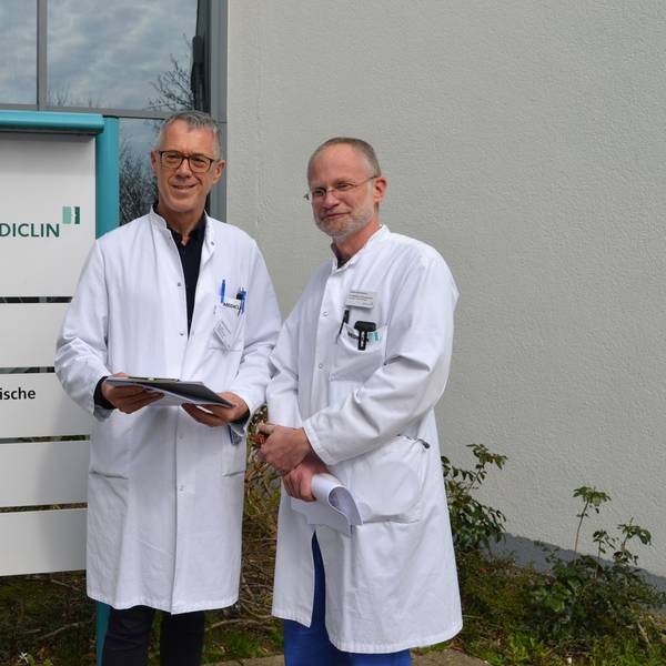 Zwei Ärzte stehen in weißen Kitteln vor dem Eingang der Mediclin-Rehaklinik in Reichshof.