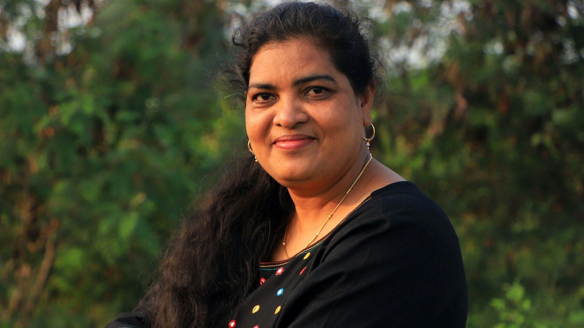 Sukirtharan, eine indische Frau mittleren Alters mit langen dunklen Haaren lehnt auf einem Pfeiler und schaut in die Kamera.