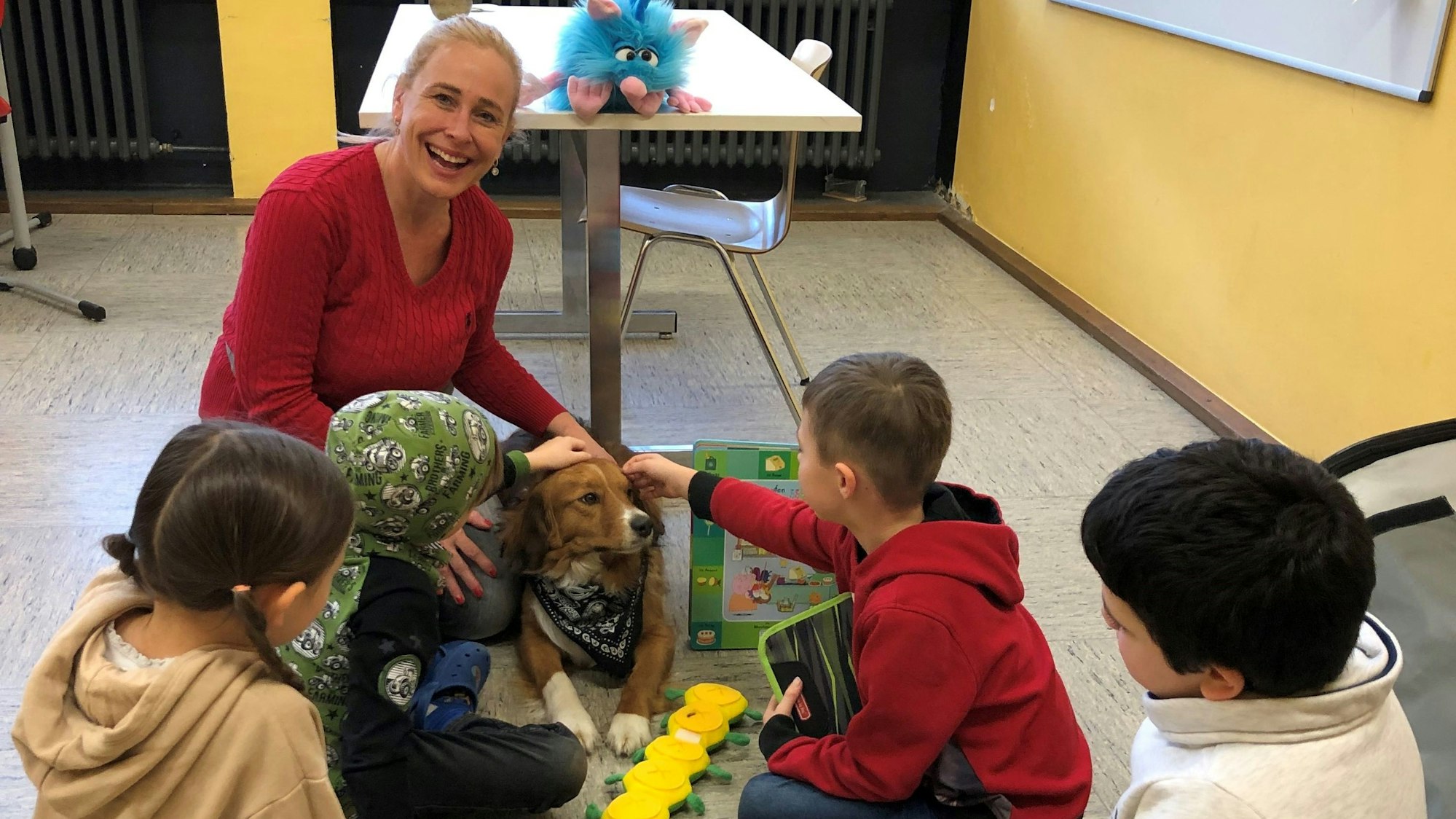 Sonja Mies sitzt auf der Erde. An ihrer Seite liegt Casper. Drei Jungs und ein Mädchen sitzen in einem Halbkreis mit ihr.