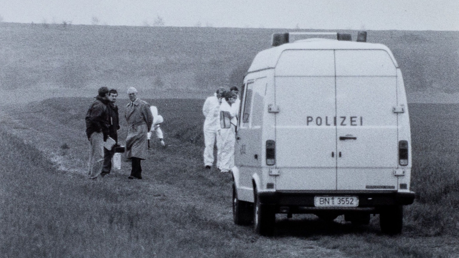 Das historische Foto zeigt einen Transporter der Polizei, der auf einem Feldweg steht. Um ihn herum stehen Menschen.