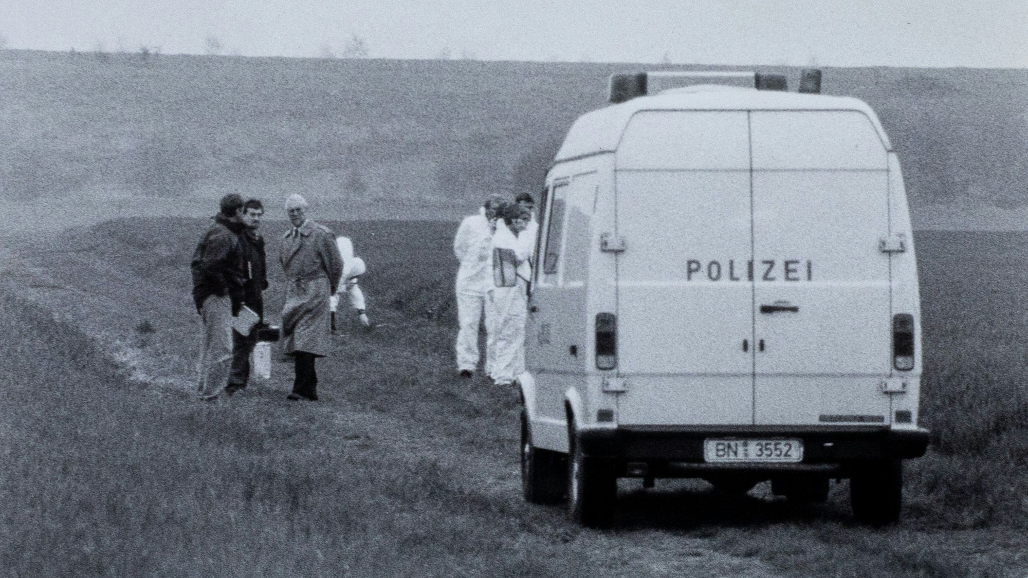 Das historische Foto zeigt einen Transporter der Polizei, der auf einem Feldweg steht. Um ihn herum stehen Menschen.