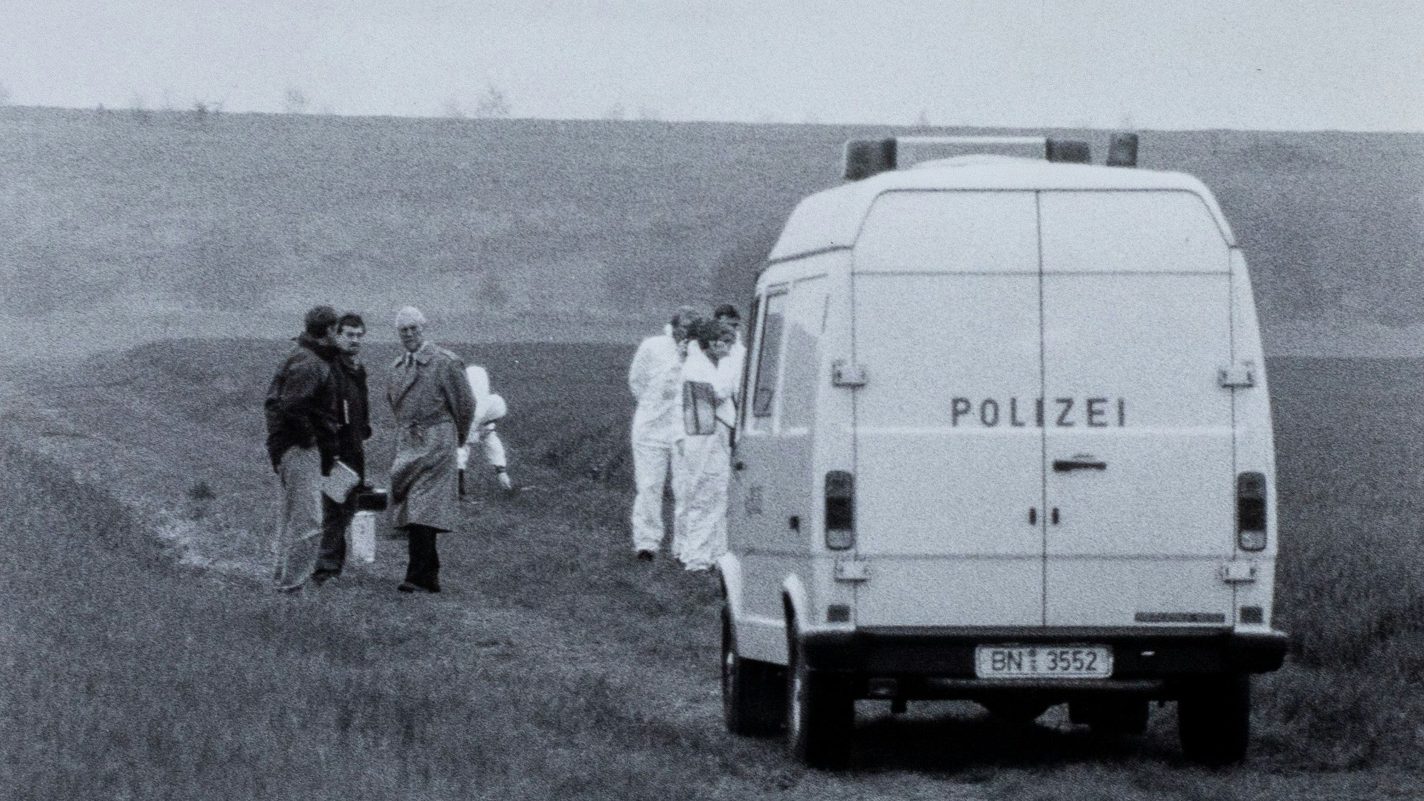 Ein Polizeiauto steht auf einem Feldweg. Das Bild ist in schwarz-weiß.