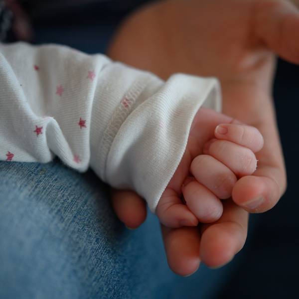 Die Hand eines zwei Wochen altes Neugeborenen liegt in der Hand seiner Mutter.