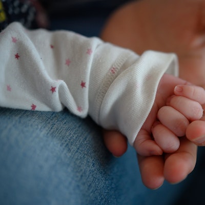 Die Hand eines zwei Wochen altes Neugeborenen liegt in der Hand seiner Mutter.