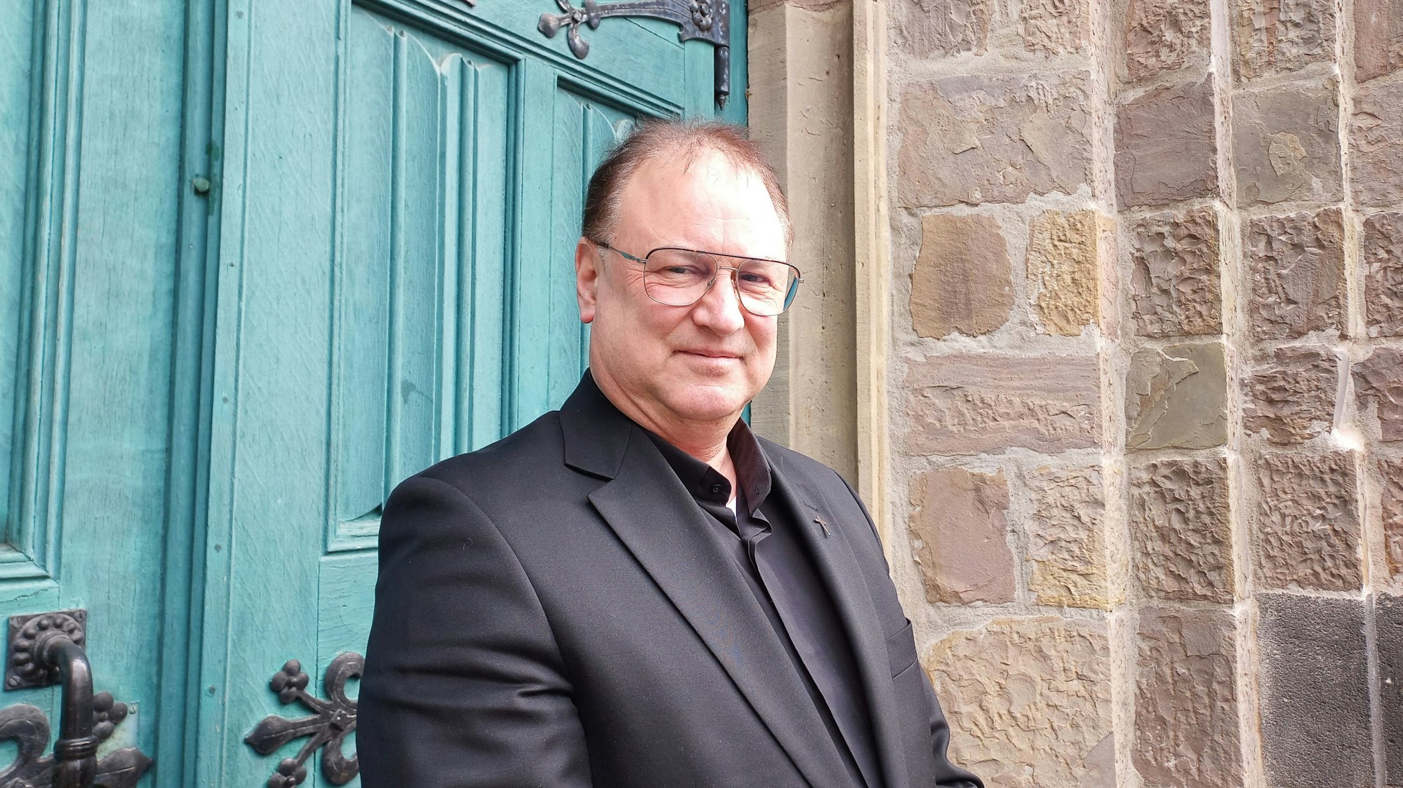 Michael Enders trägt einen schwarzen Anzug, ein schwarzes Hemd und lächelt in die Kamera.