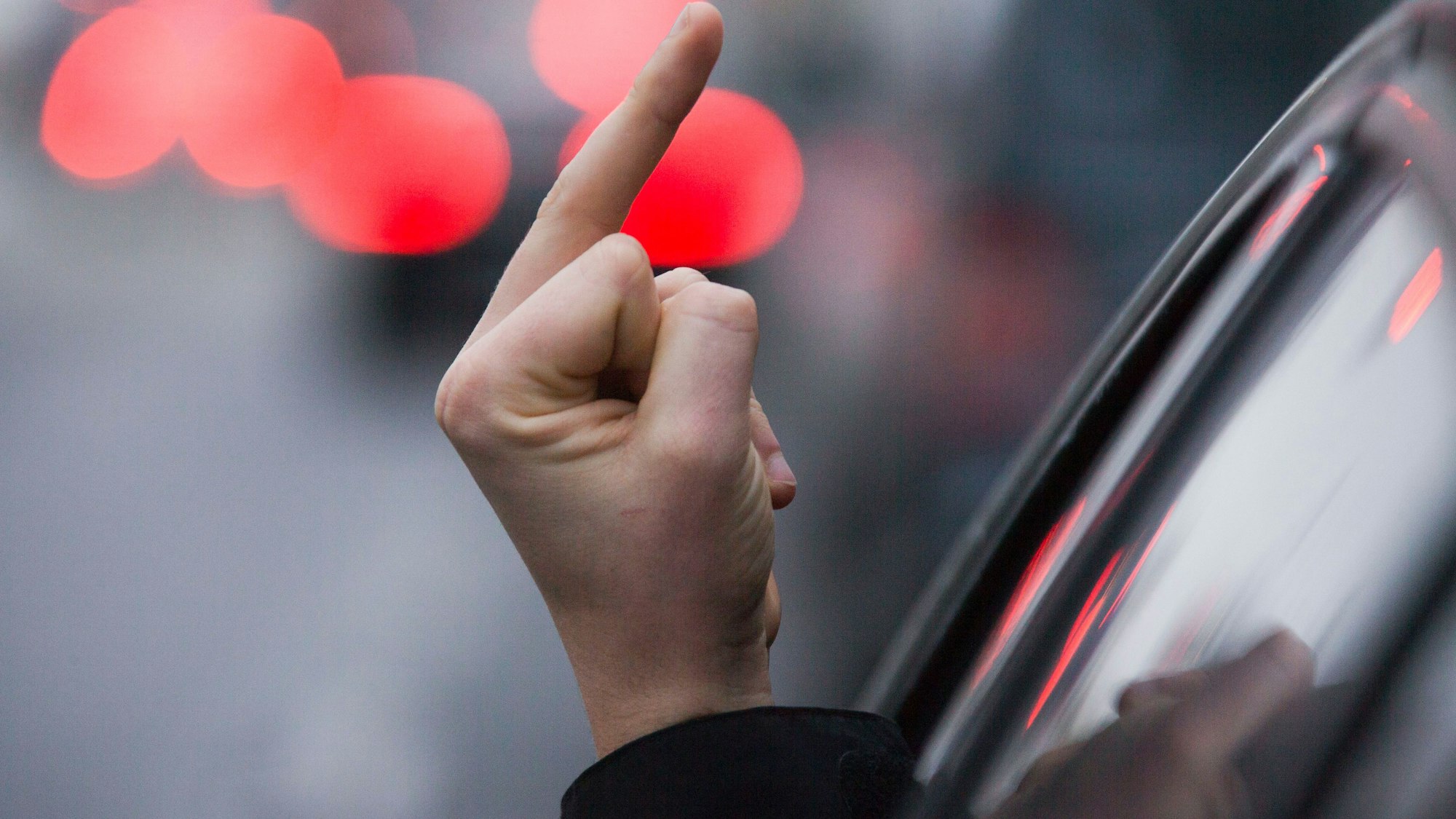 Ein Autofahrer streckt die Hand aus dem Fenster und zeigt den Mittelfinger.