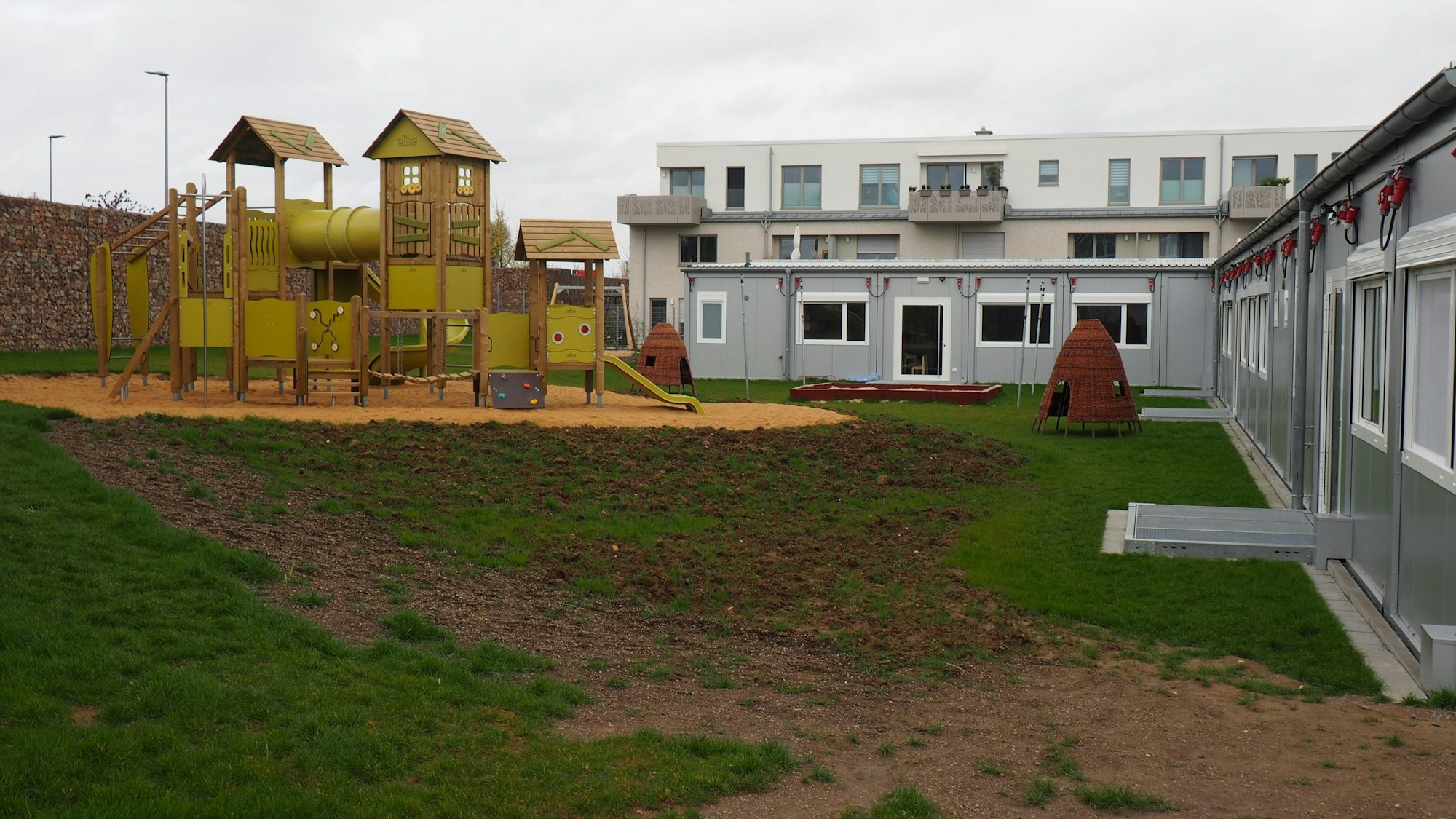Das Foto zeigt die Kita in Containerbauweise und ein Klettergerüst aus Holz.