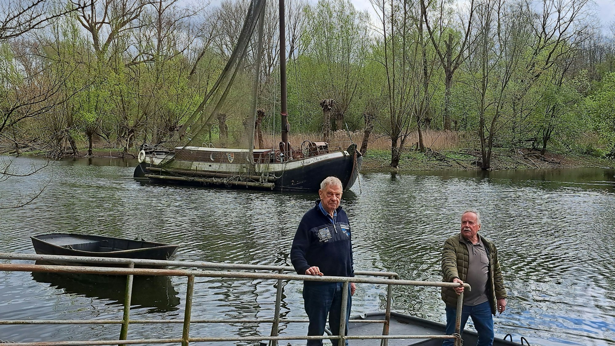 Die zwei Männer stehen am Wasser. Im Hintergrund ist das Schiff zu sehen.