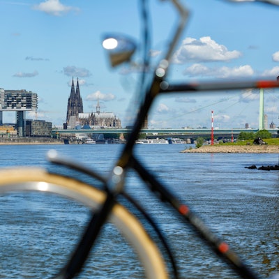 Fahrrad unscharf im Vordergrund vor Köln Kulisse mit Kranhäusern und Dom