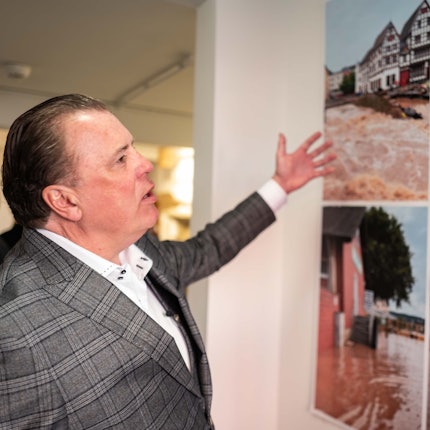 Marc Brucherseifer, Geschäftsführer des City Outlets, deutet auf einige Bilder, die nach der Flutkatastrophe in Bad Münstereifel entstanden sind.