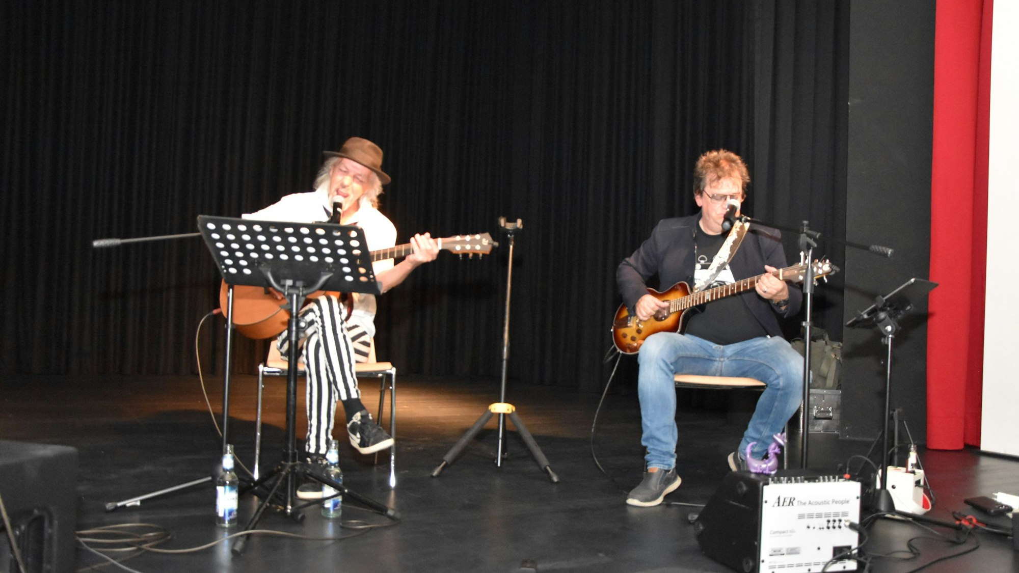 Phil Wolff (l.) und Dieter Kirchenbauer sitzen auf zwei Stühlen auf der Bühne und spielen Gitarre.
