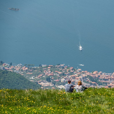 Blick vom Berg Monte Baldo auf den Gardasee und den Ort Malcesine. Auf dem See ist ein weißes Boot unterwegs.