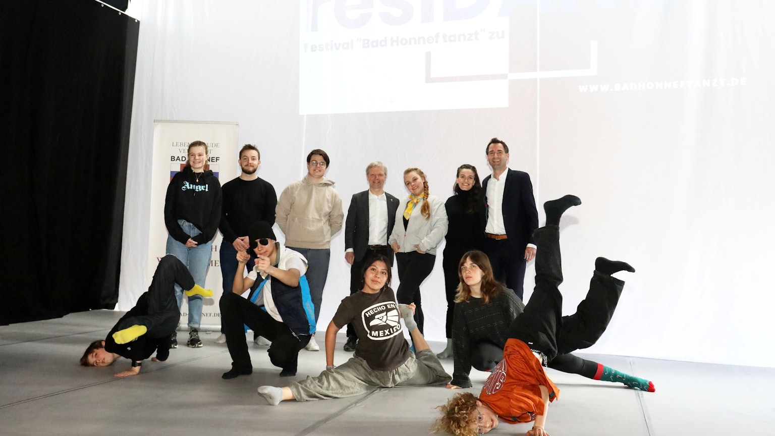 Eine Gruppe von Menschen steht im Ratssaal vor einer weißen Wand. Einige Kinder und Jugendliche zeigen Tanz-Elemente, wohl aus Rap oder Breakdance.