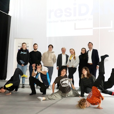 Eine Gruppe von Menschen steht im Ratssaal vor einer weißen Wand. Einige Kinder und Jugendliche zeigen Tanz-Elemente, wohl aus Rap oder Breakdance.