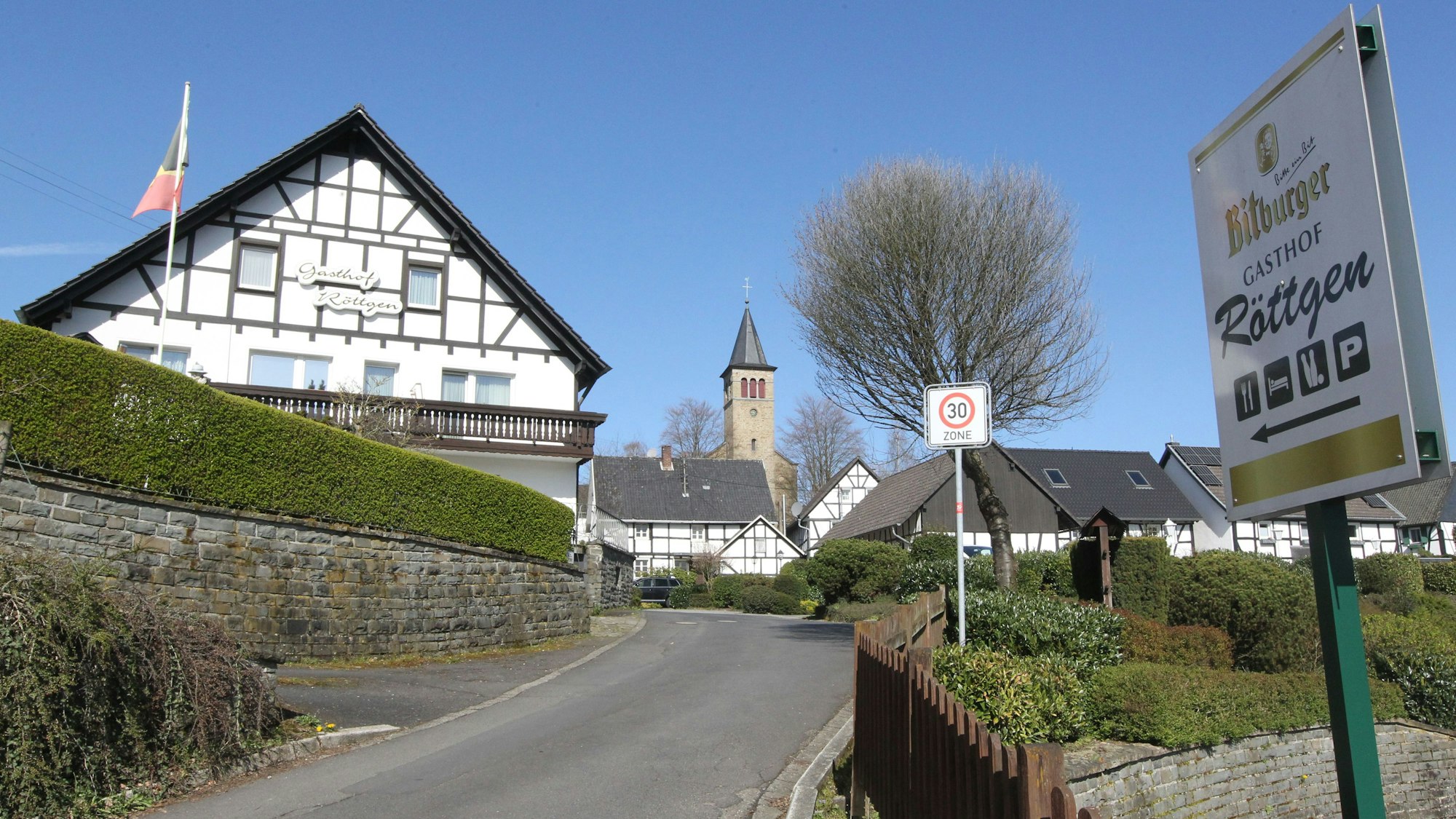 Ein Fachwerkhaus liegt an einer Straße, im Hintergrund ist eine Kirche zu sehen.