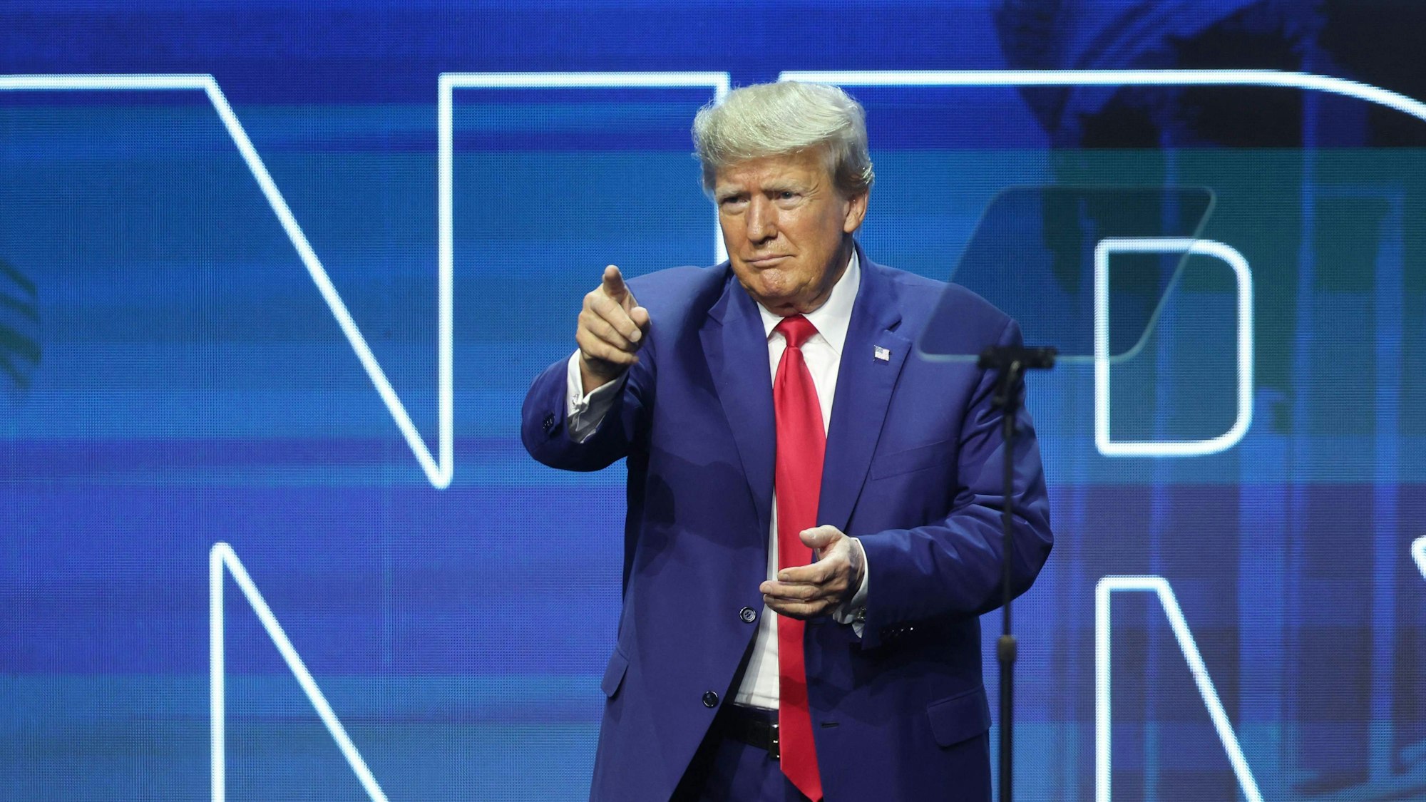 Es ist Donald Trump auf einer Bühne zu sehen. Er zeigt mit seinem Finger ins Publikum.