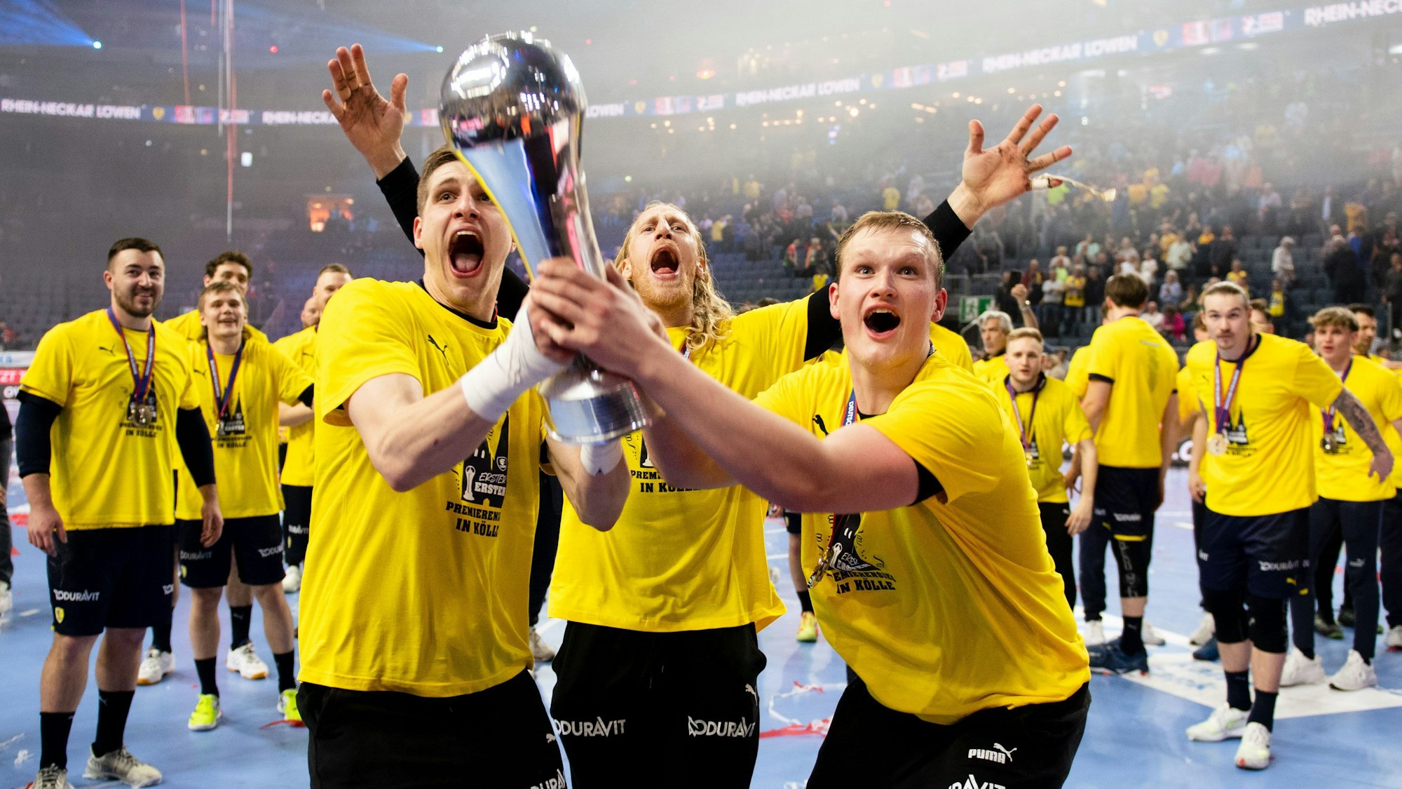 Spieler der Rhein-Neckar Löwen feiern gemeinsam mit dem Pokal in der Hand. Sie tragen gelbe T-Shirts.