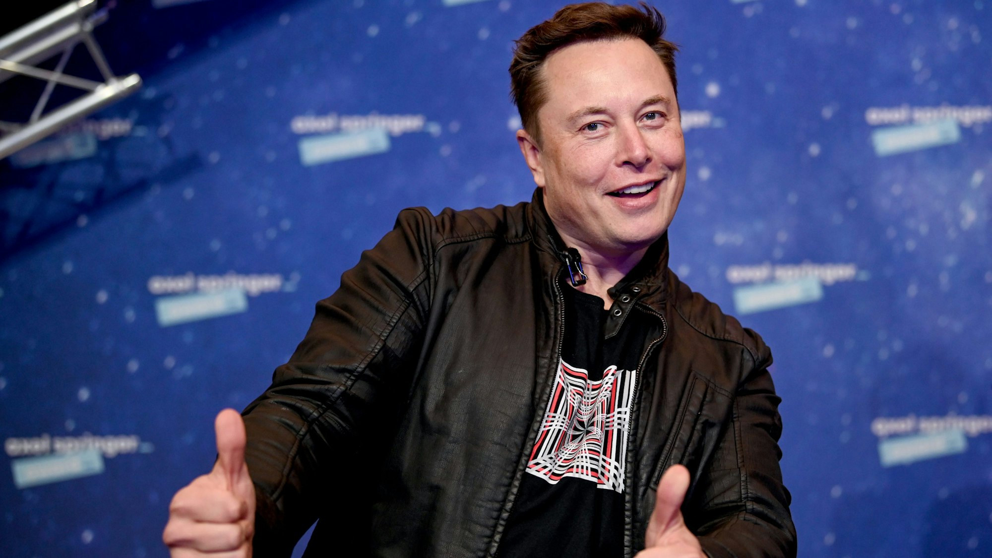 Elon Musk, Chef der Weltraumfirma SpaceX und Tesla-CEO, kommt zur Preisverleihung des Axel Springer Award. Er trägt eine dunkle Lederjacke und hält seine Daumen in die Kamera.