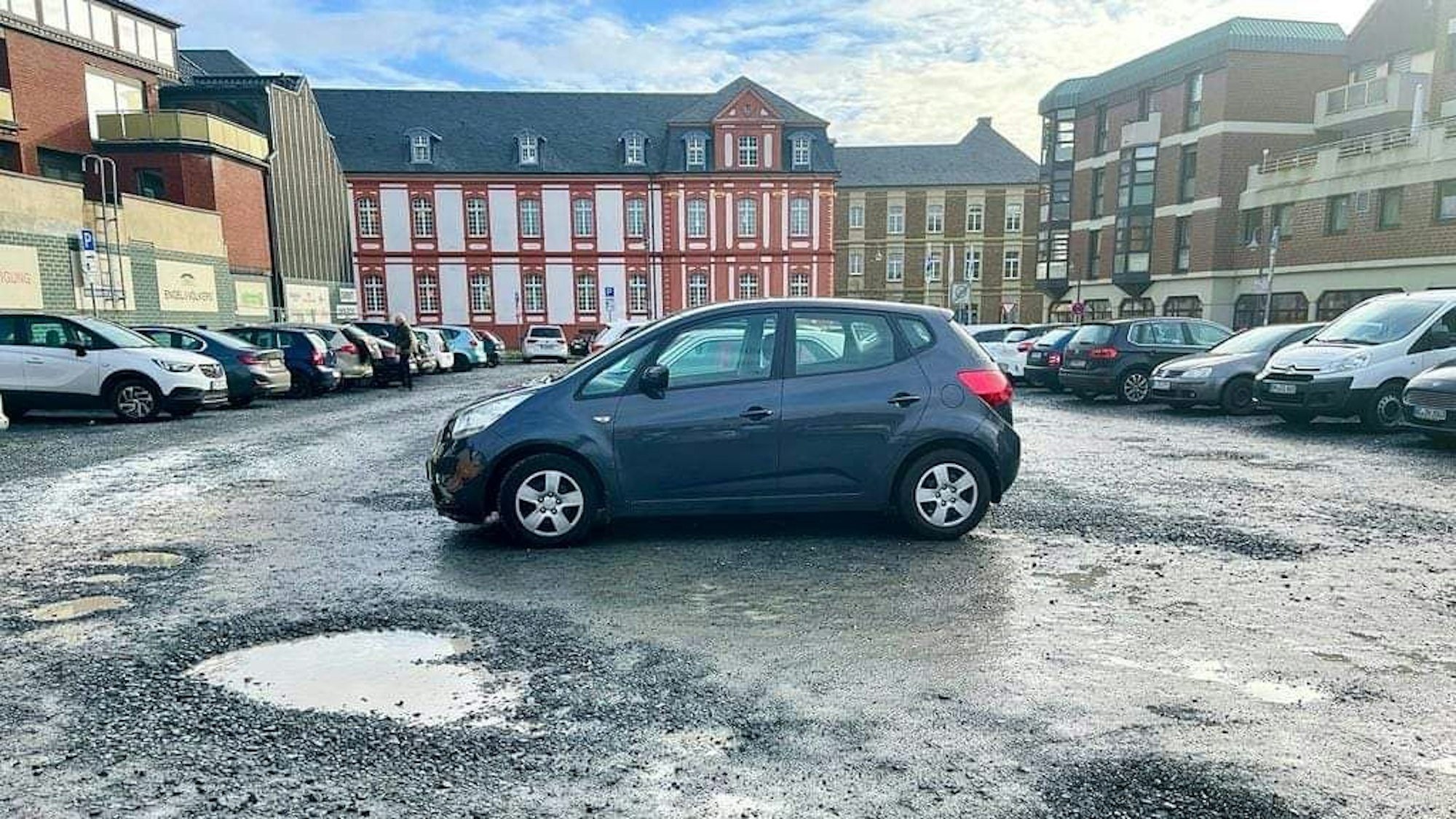 Das Foto zeigt den Schotterparkplatz an der Kaiser-Otto-Straße/Ecke Ehrenfriedstraße. Bei Regen bilden sich Pfützen, im Sommer staubt es.