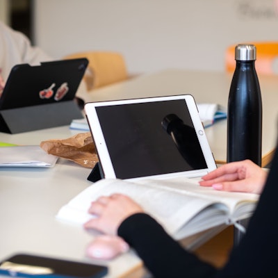 Eine Schülerin hat ein Buch und ein iPad vor sich auf dem Tisch liegen.