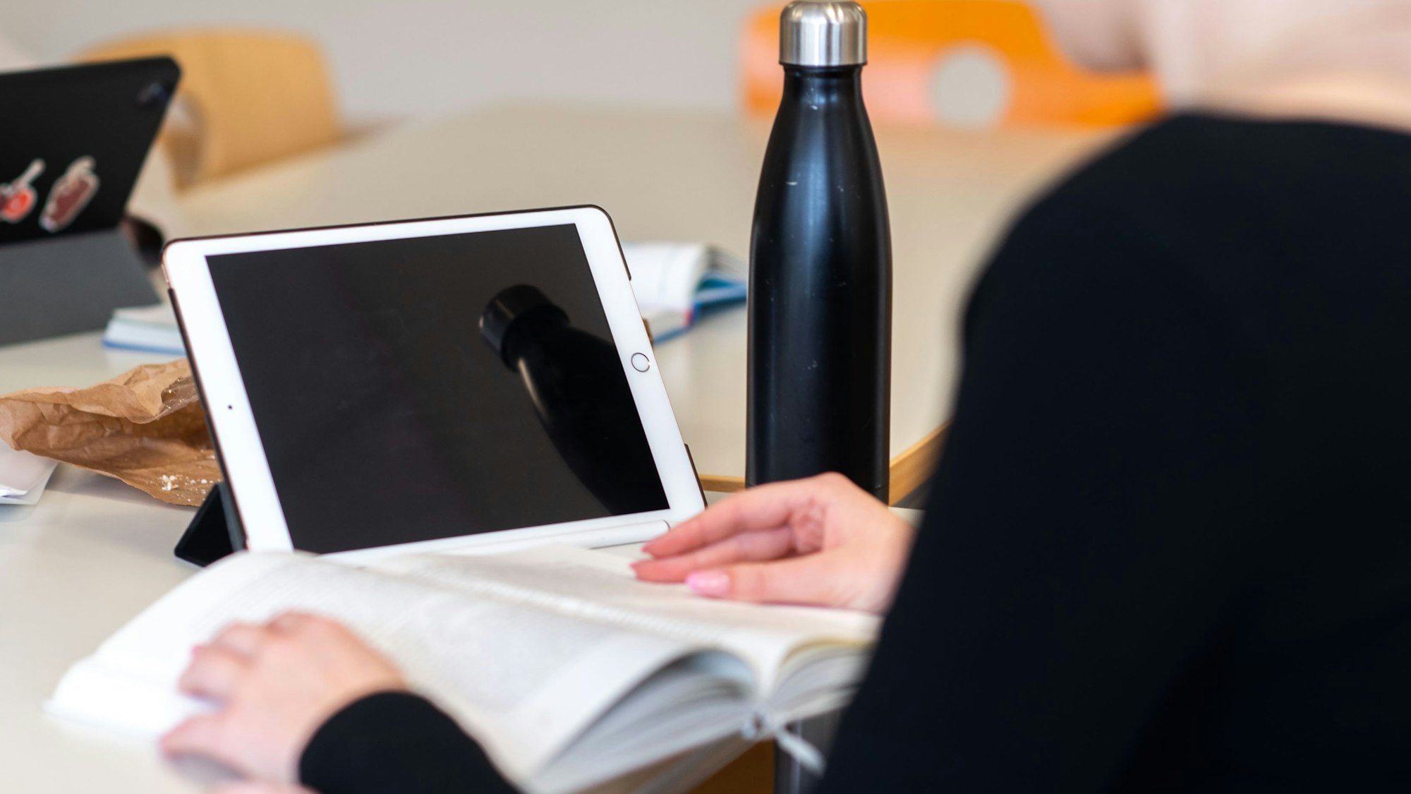 In der Marienschule in Euskirchen arbeitet eine Schülerin mit Buch und Tablet. Auf dem Tisch steht auch eine Trinkflasche.