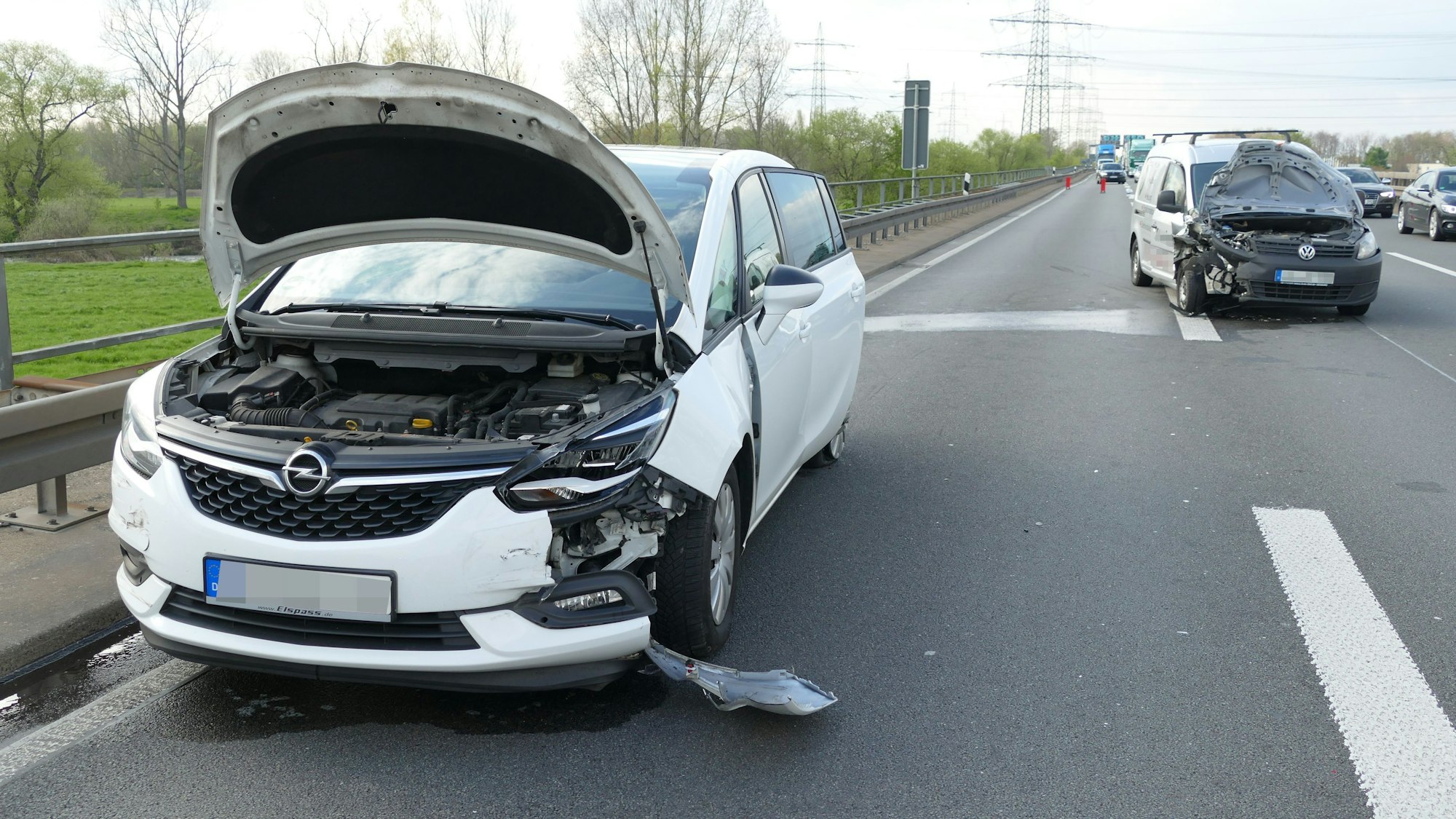 Ein demoliertes Auto steht mit offener Motorhaube am Straßenrand, dahinter steht ein weiteres Auto, ebenfalls mit offener Motorhaube.