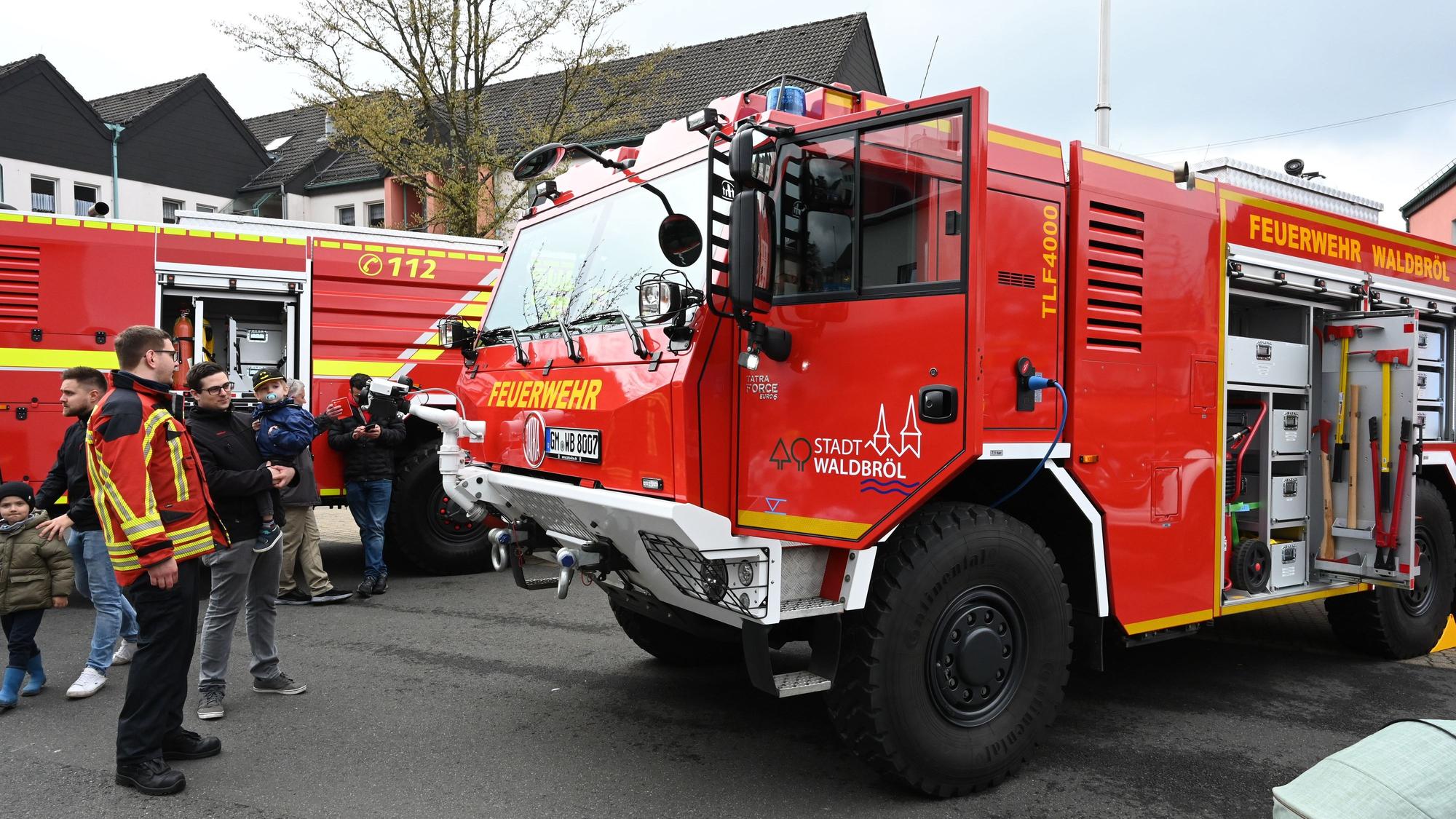Es ist ein Fahrzeug der Waldbröler Feuerwehr zu sehen. Neben diesem stehen mehrere Menschen.