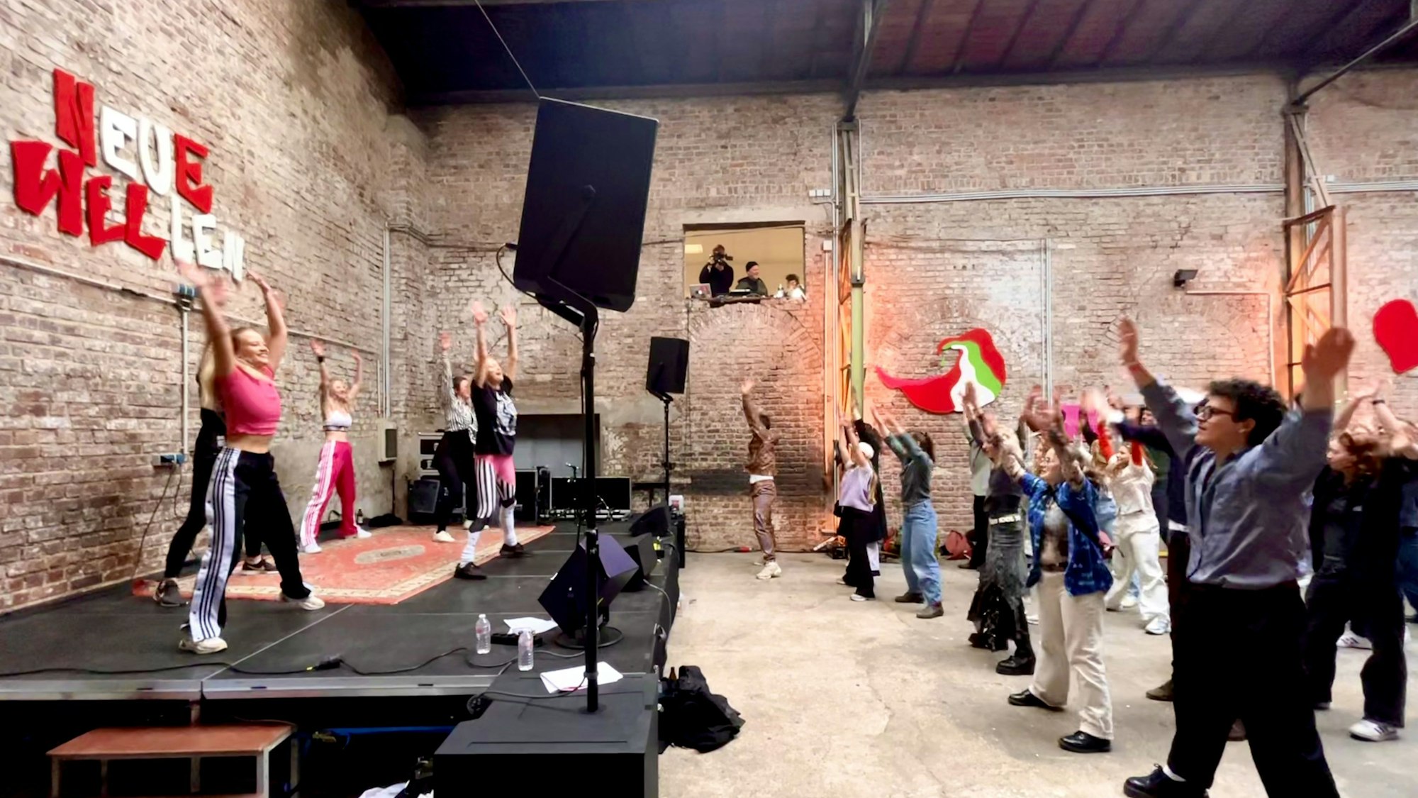 Besucher des Neue Wellen Festival tanzen in einer der alten Hallen vor einer Bühne.