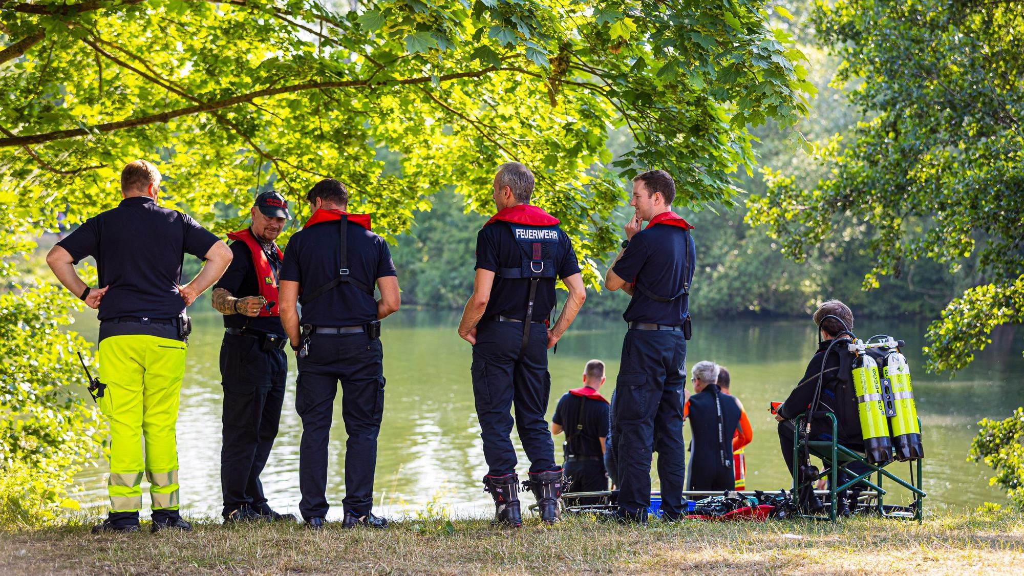 Feuerwehrleute und DLRG-Kräfte stehen bei einem Einsatz an einem See.