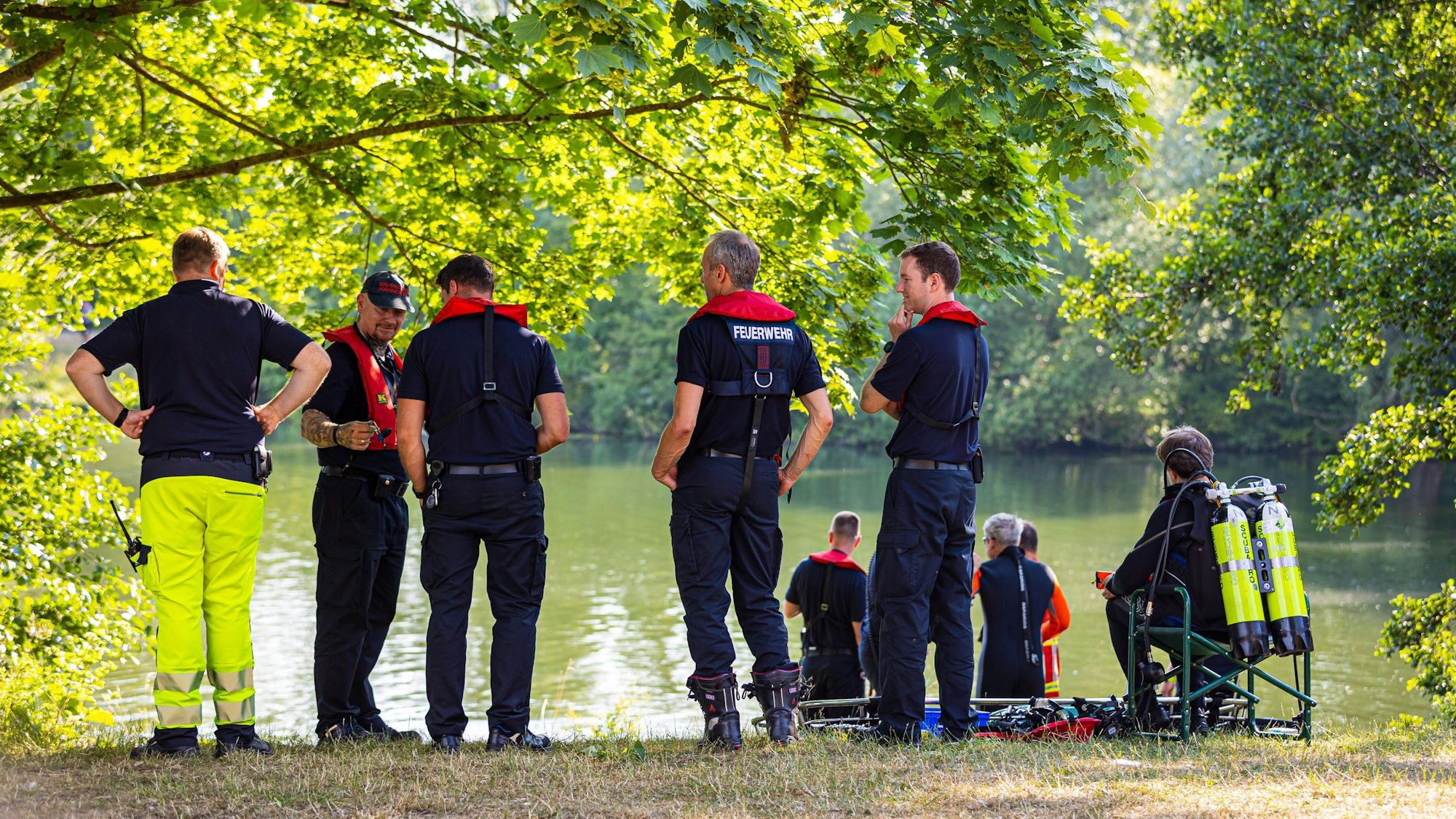 Feuerwehrleute und DLRG-Kräfte stehen bei einem Einsatz an einem See.