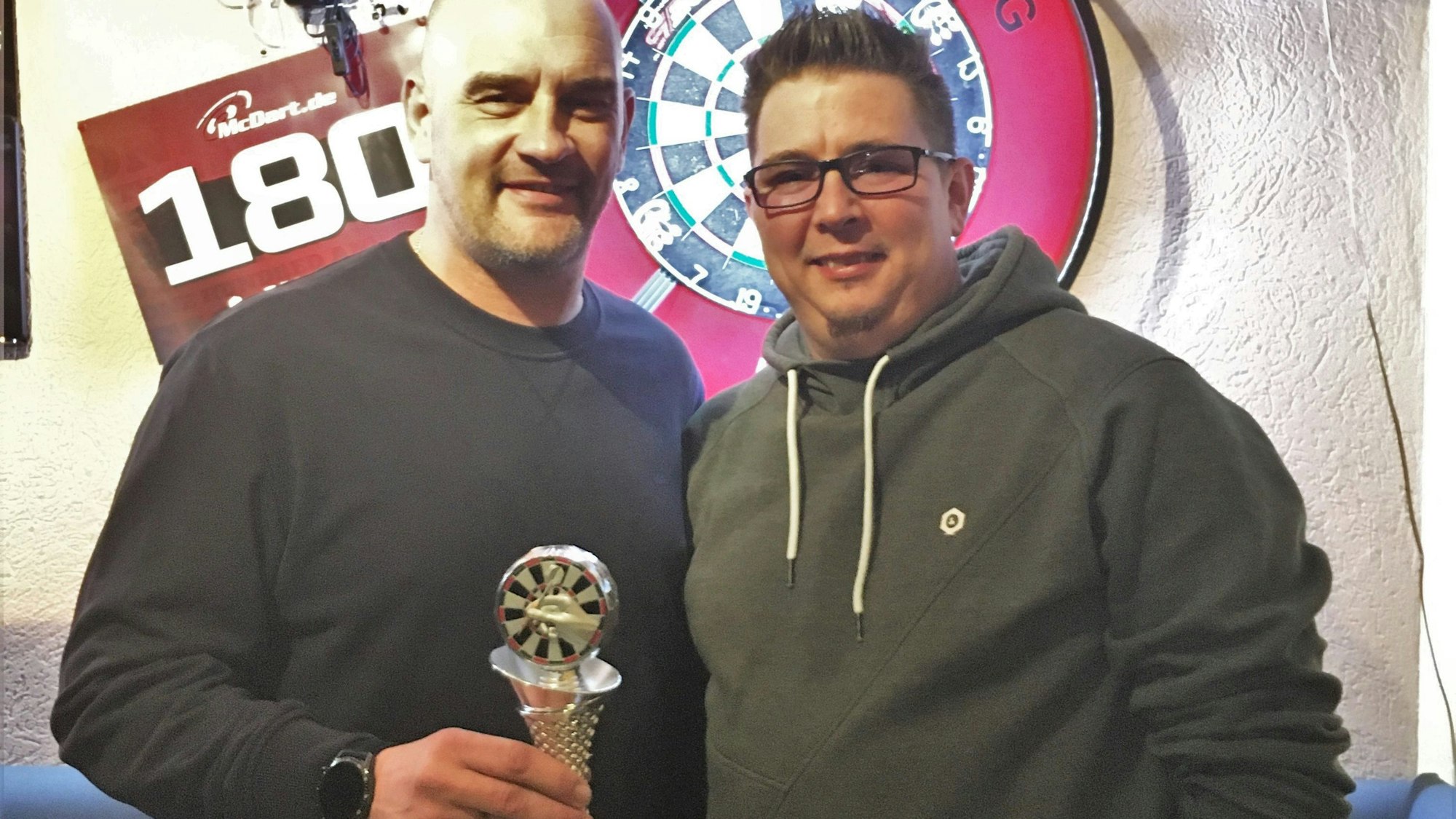 Blick auf zwei Dartspieler mit Pokal.