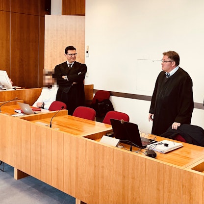 Angeklagte und Verteidiger sitzen und stehen im Gericht.