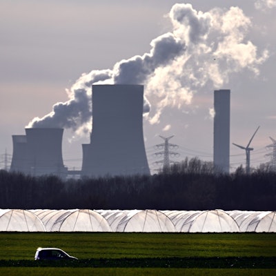 Ein Auto fährt im Sonnenschein an Gewächshäusern vor dem Braunkohlekraftwerk Niederaußem vorbei.