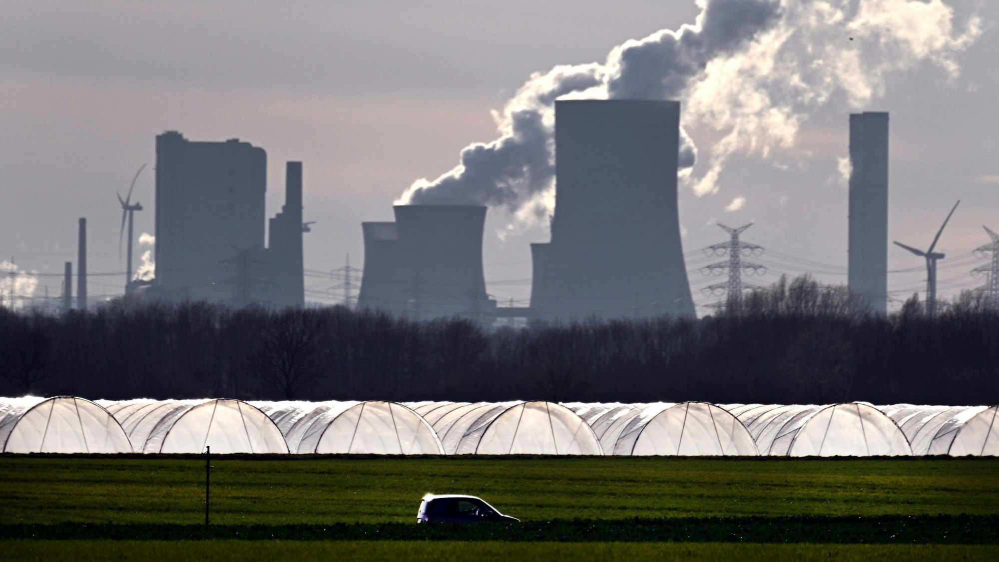 Ein Auto fährt im Sonnenschein an Gewächshäusern vor dem Braunkohlekraftwerk Niederaußem vorbei.