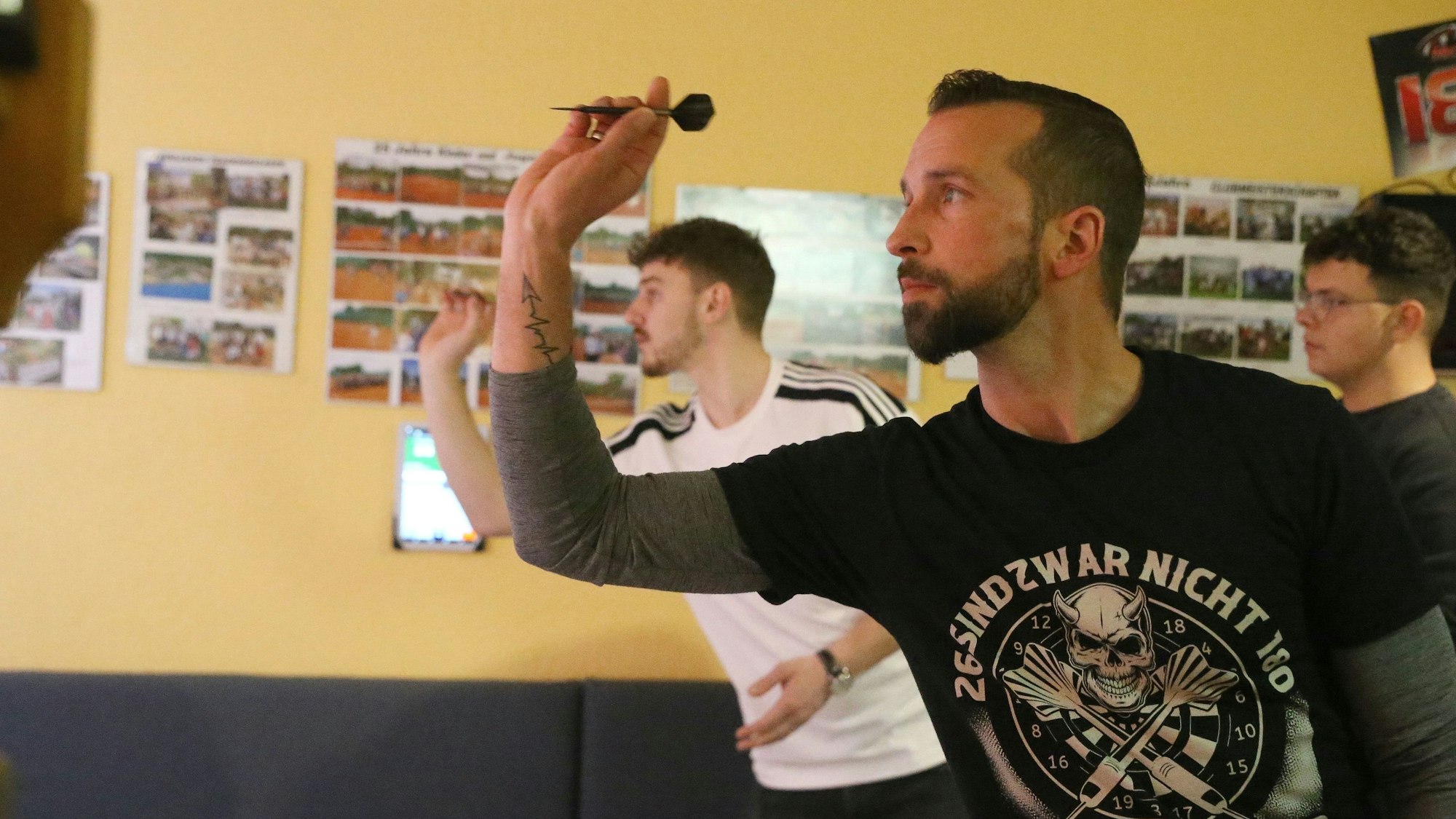 Zu sehen ist ein Dartspieler, der mit dem Pfeil zielt.