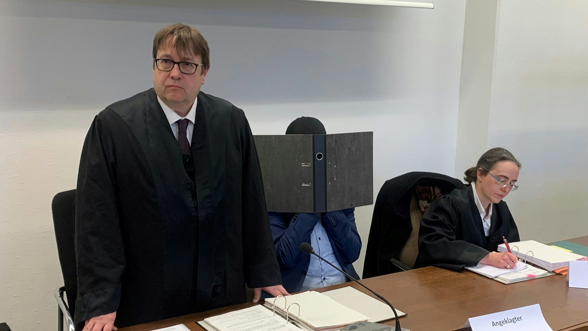 Der Angeklagte verbirgt sein Gesicht hinter einem Aktenordner